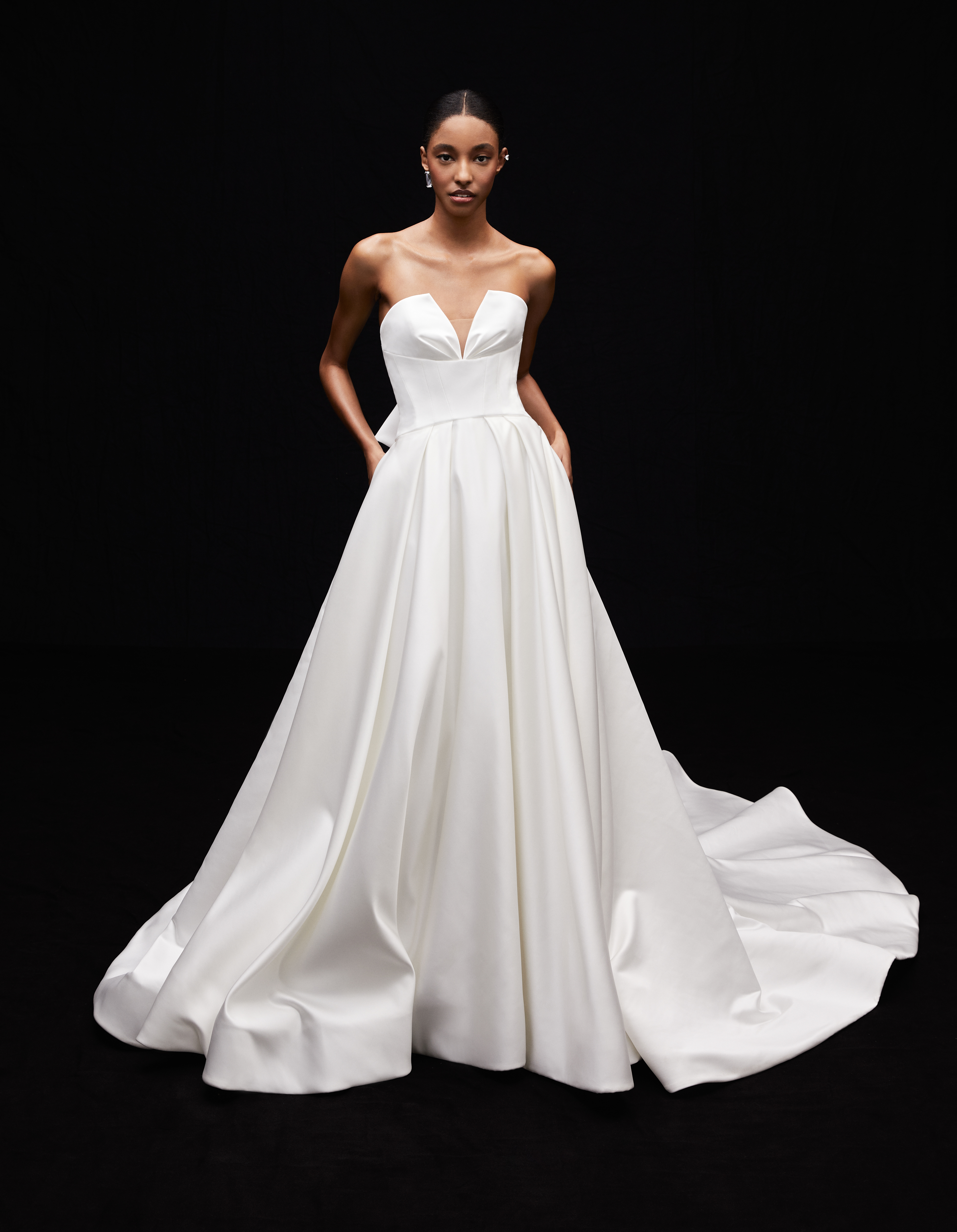 Demi satin ball gown with draped corset bodice, empire detail, pockets, and tuxedo back bow, shown from the front.