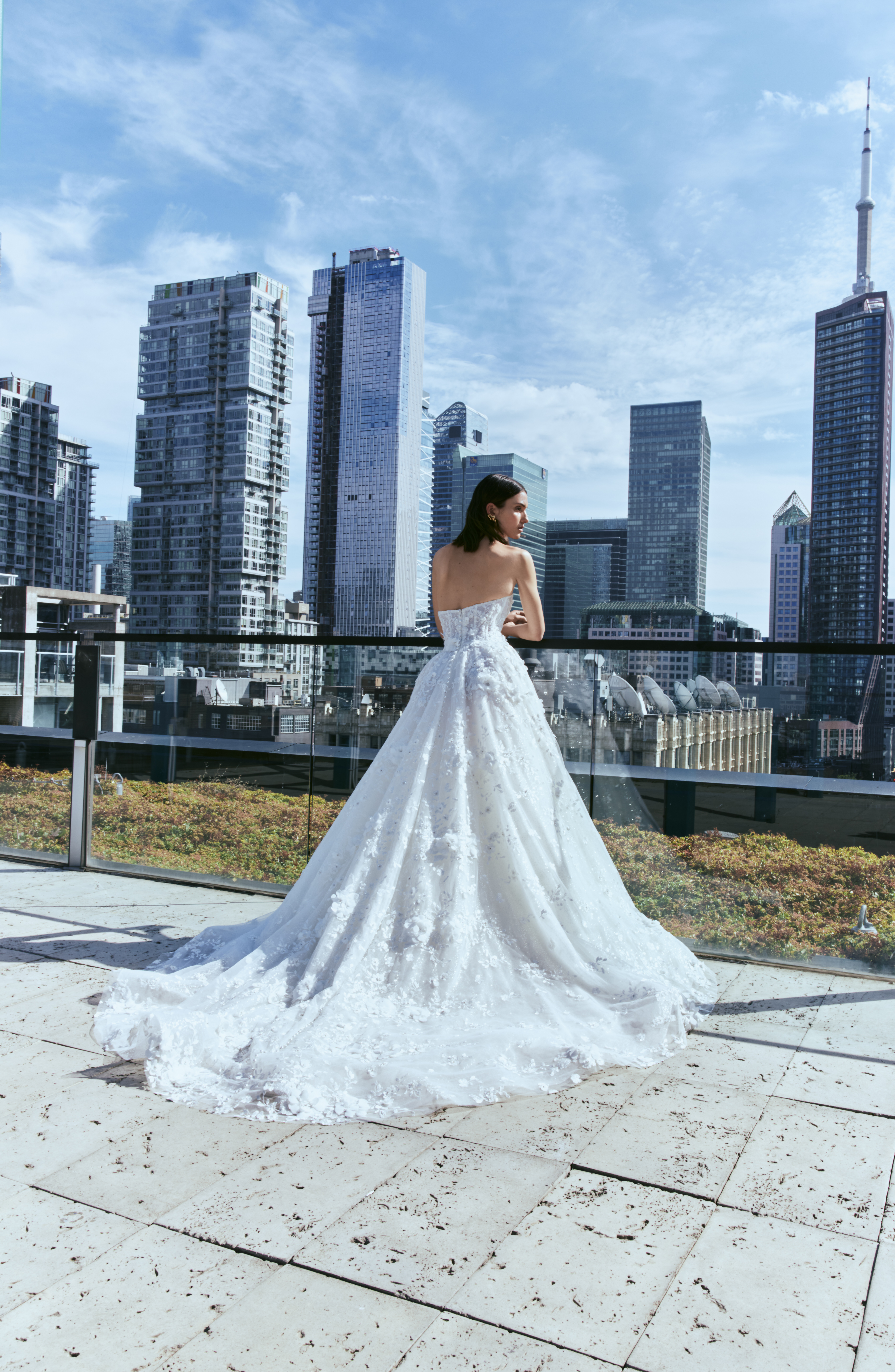 Bride wearing the James ballgown with a long train, standing outdoors by the city skyline.