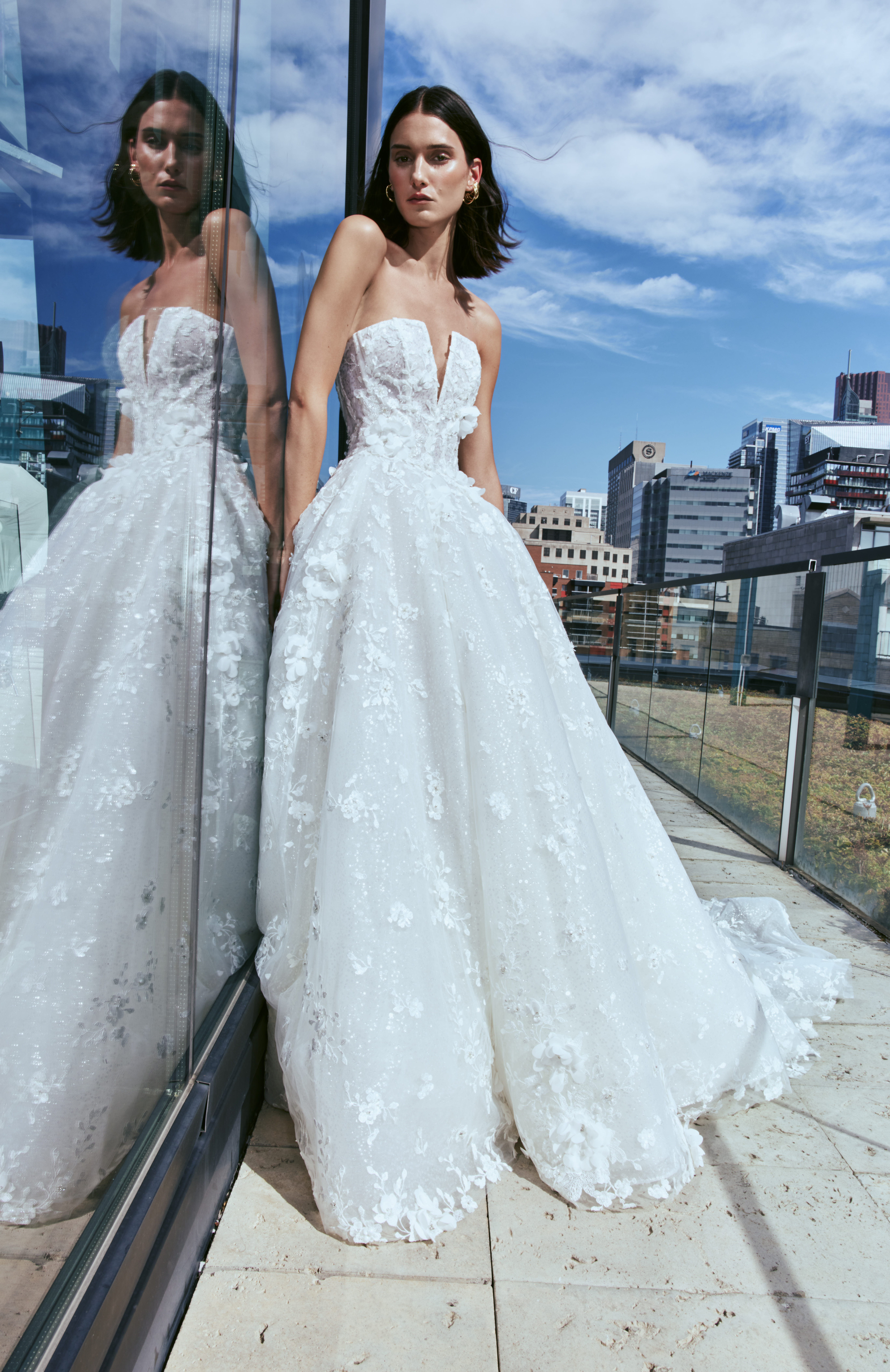 Bride wearing the James ballgown with a long train, standing outdoors by the city skyline.