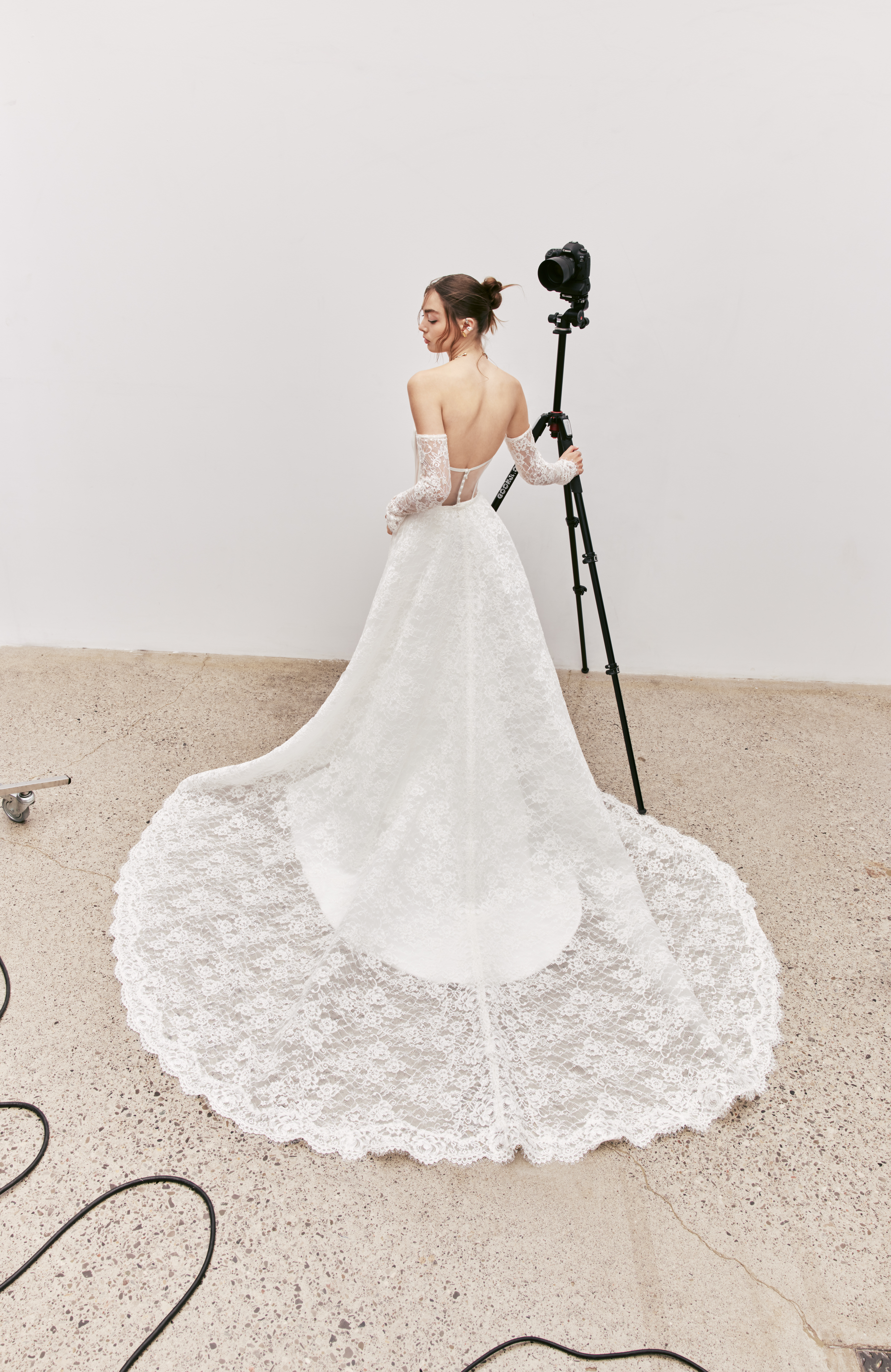 Back view of Rori strapless fit-and-flare gown with exposed boning detail, corded lace overskirt, and sleeves.