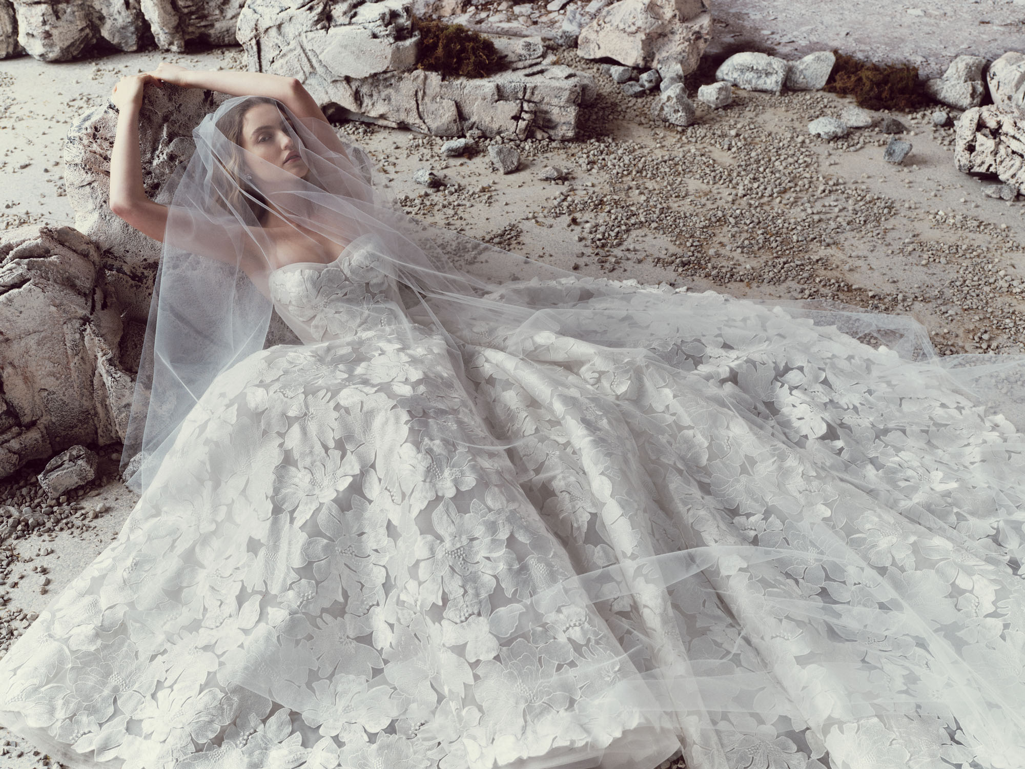 Fiora RIVINI SS27 ball gown shown seated, with a translucent corset bodice and voluminous floral lace skirt spread around her.