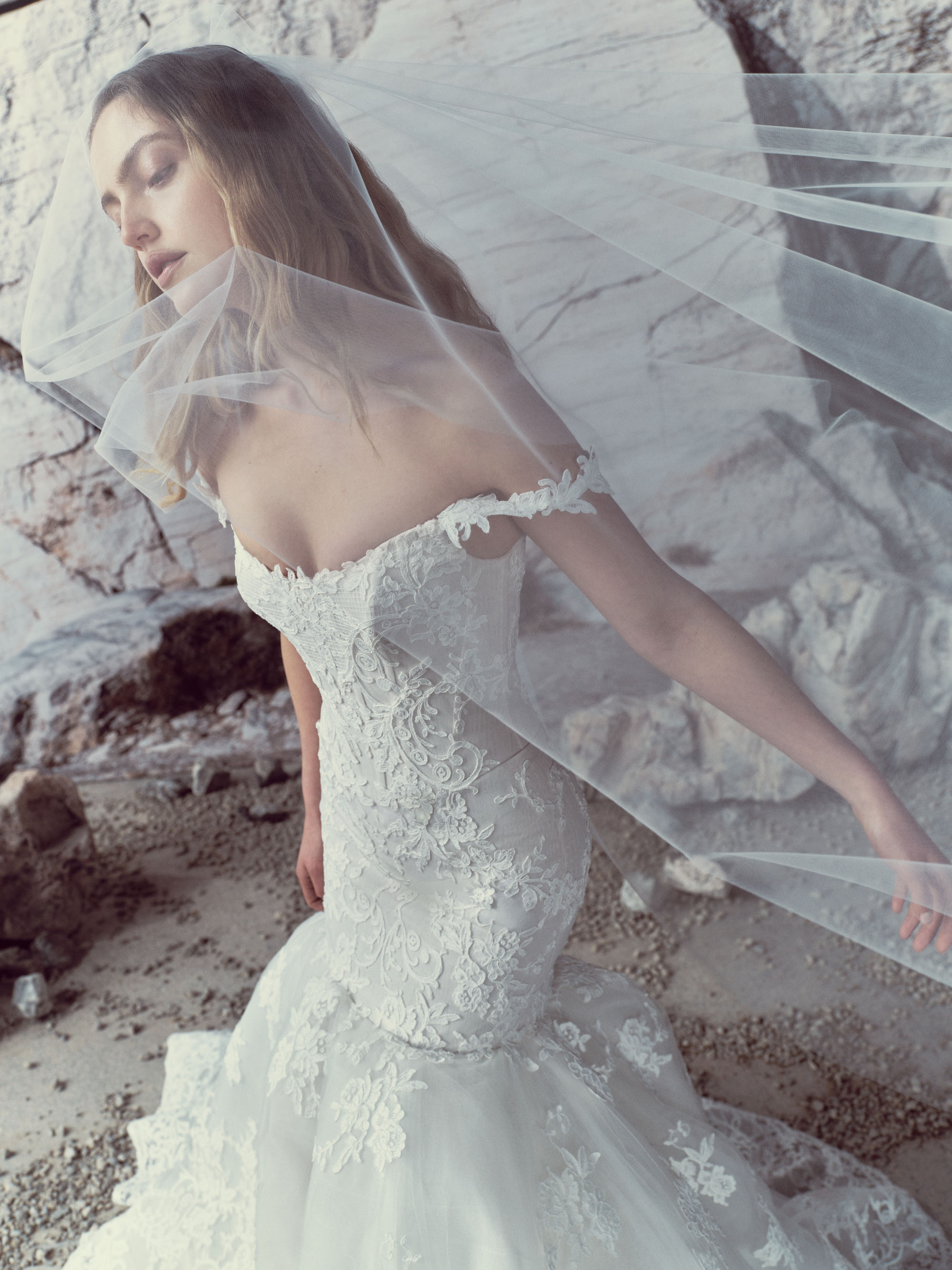 Maren RIVINI SS27 elongated mermaid gown in hand-applied Alençon lace with an off-the-shoulder floral strap and sculptural tulle skirt.