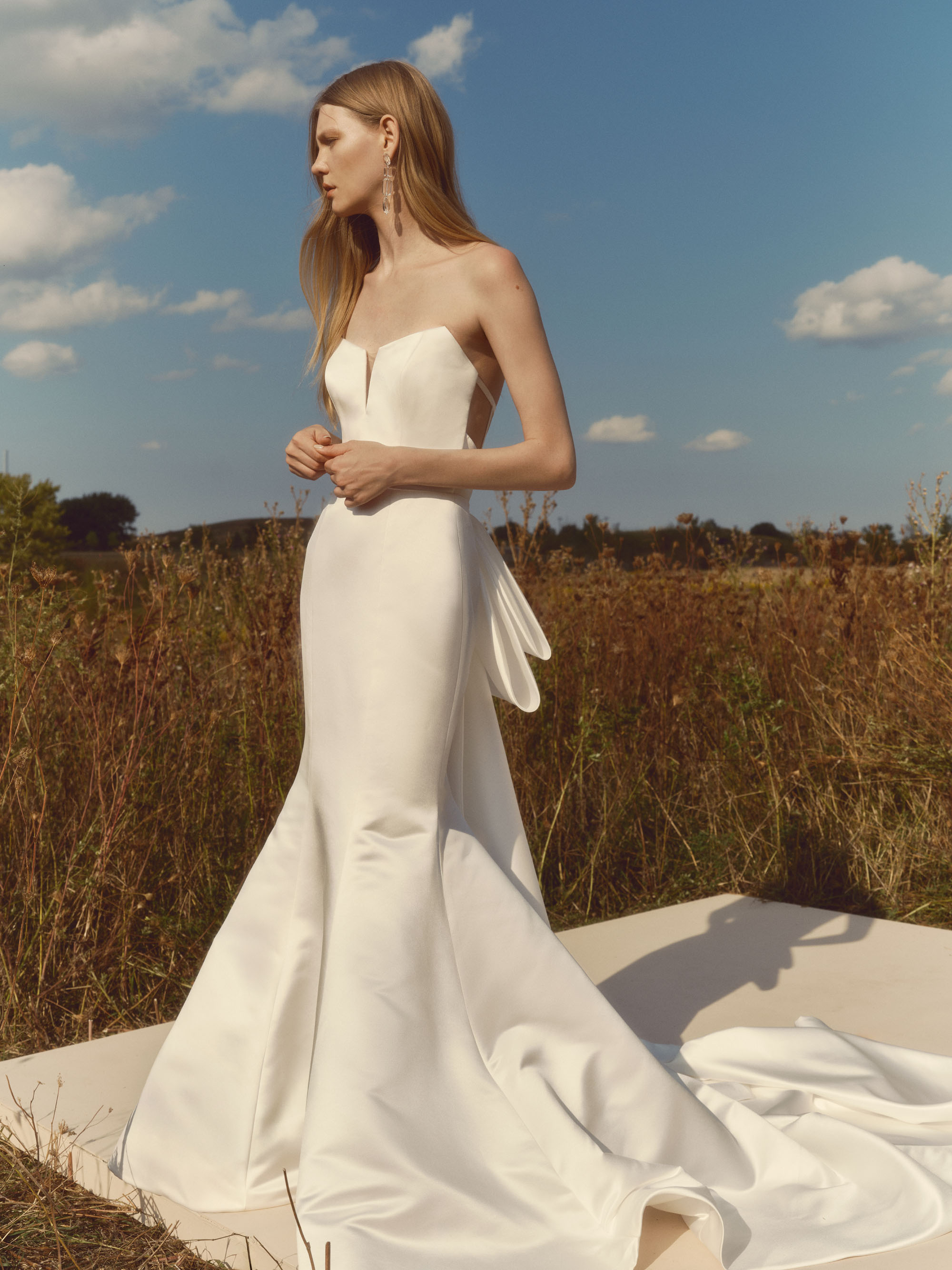 Echo cat-eye strapless fit-and-flare satin gown with a sleek bodice, oversized back bow, and trailing tails, shown from the side.