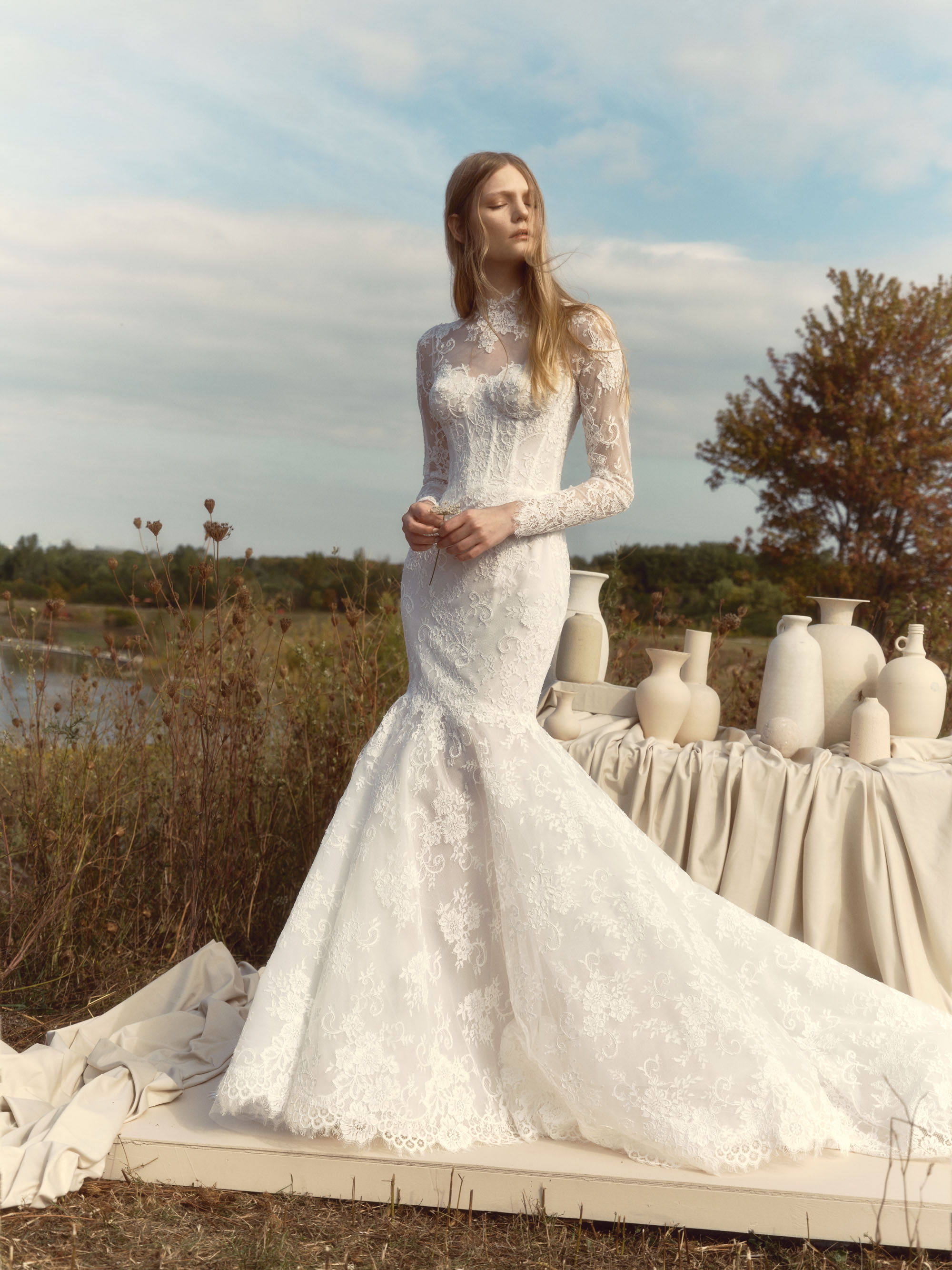 Fawn long-sleeve lace mermaid gown with illusion high neckline, sheer corseted bodice, and flowing skirt, shown from the front.
