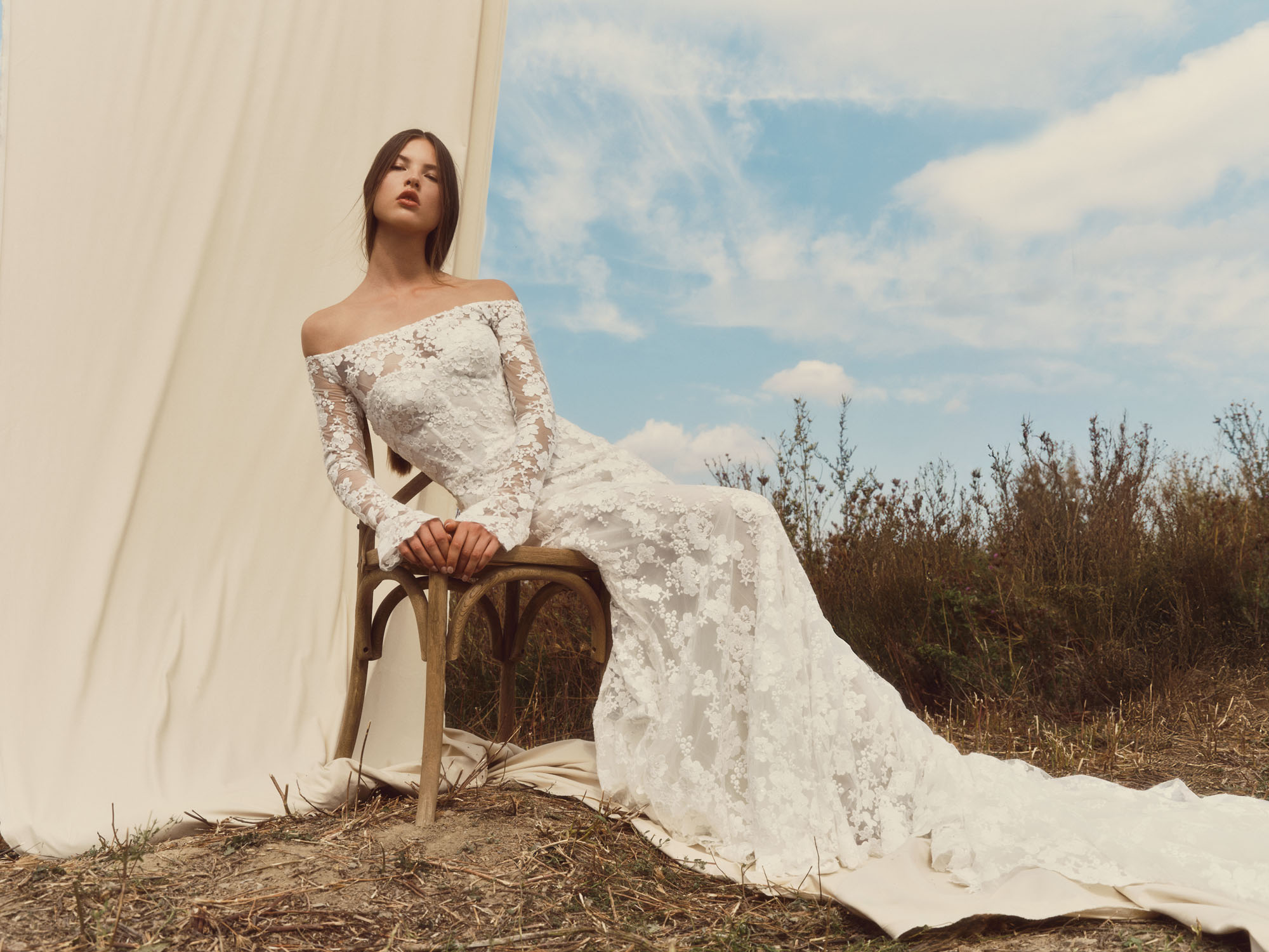 Halo strapless corseted sheath gown in beaded laser-cut floral lace with detachable long-sleeve bolero, shown seated outdoors.