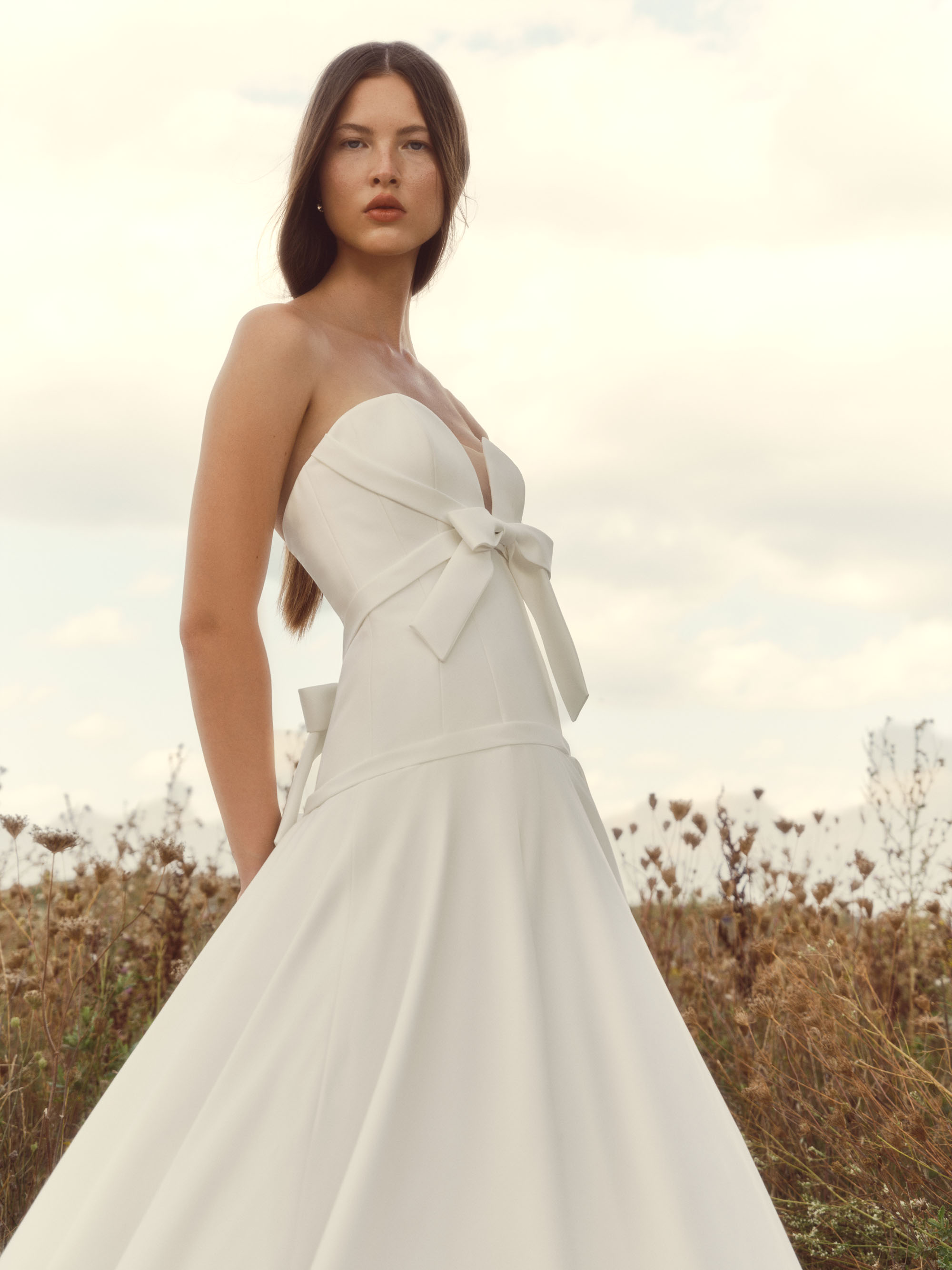 Pearl strapless ball gown with sculpted sweetheart bodice, soft bias bands, delicate front bows, and a full airy skirt, shown from the front.