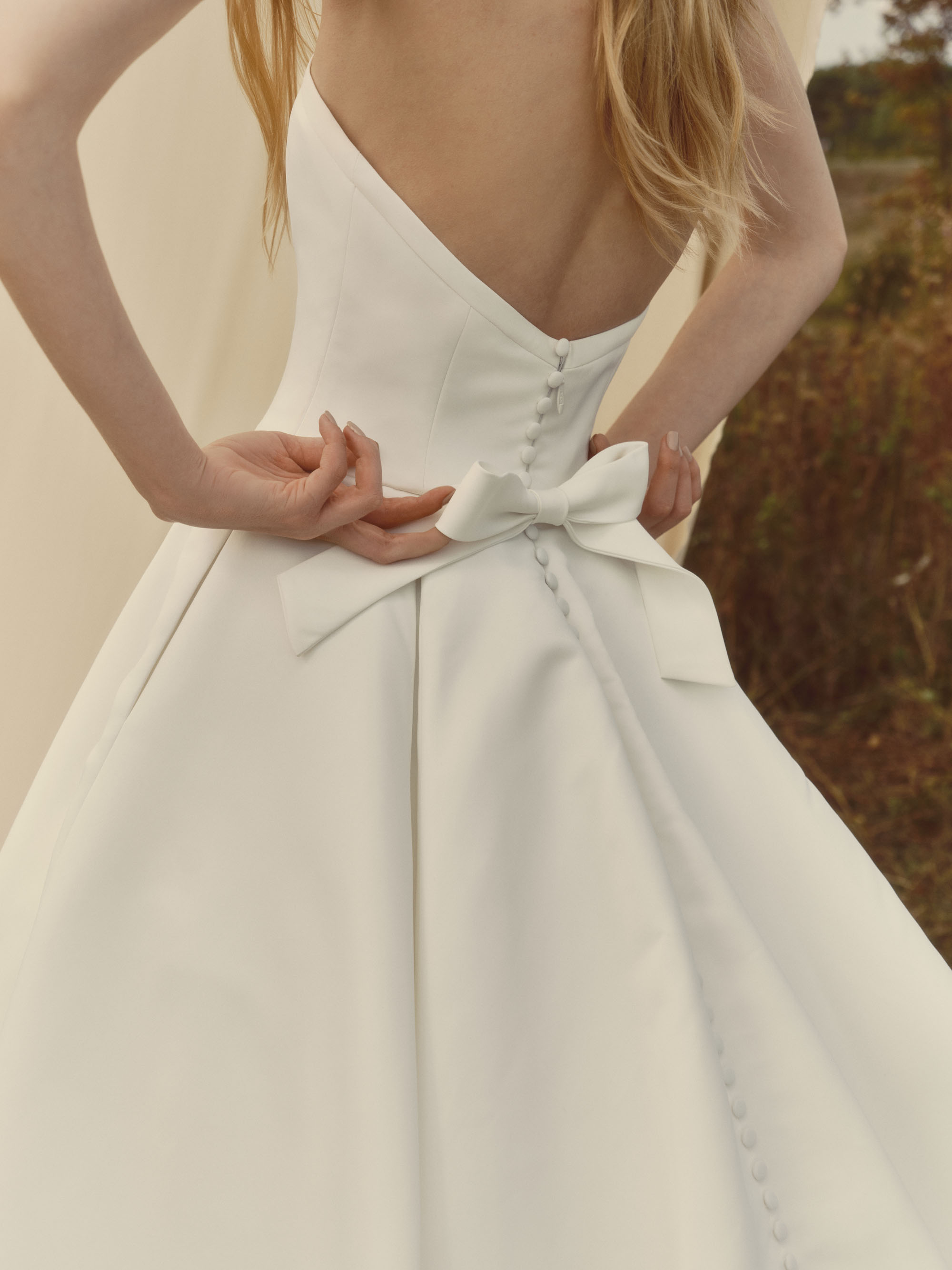 Close-up of Serene showing the plunging neckline, sculpted matte satin bodice, and delicate waist bow detail.