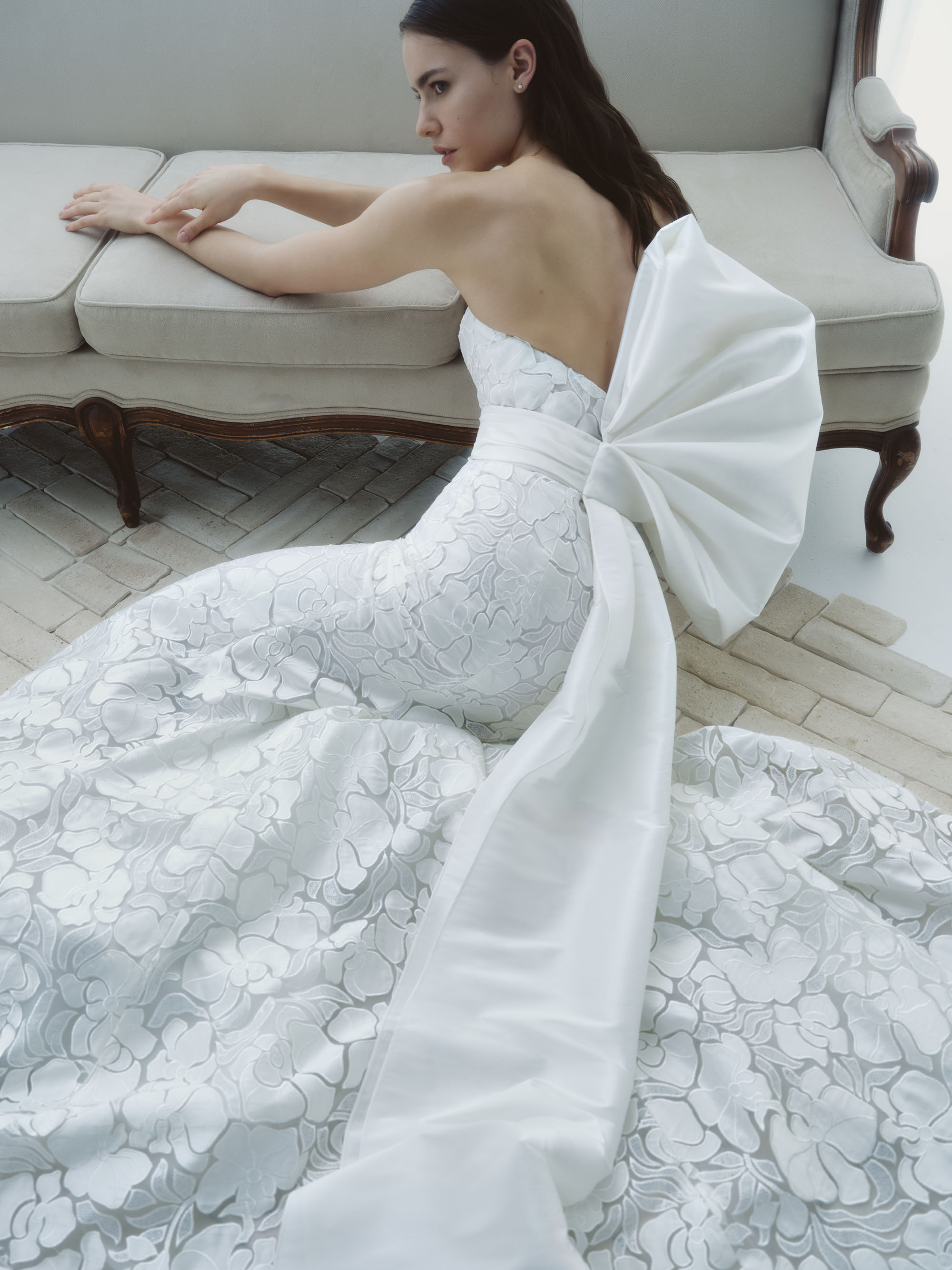 Essence shown seated, highlighting the airy beaded lace skirt, fitted silhouette, and sculpted waist bow.
