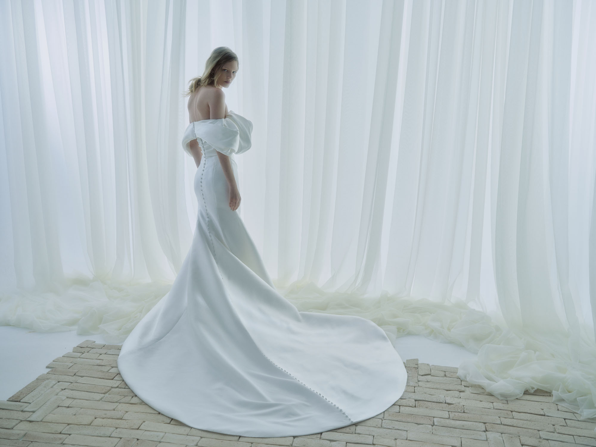 Side view of Poise showing the sleek fit-and-flare silhouette, softly draped skirt, and flowing train.