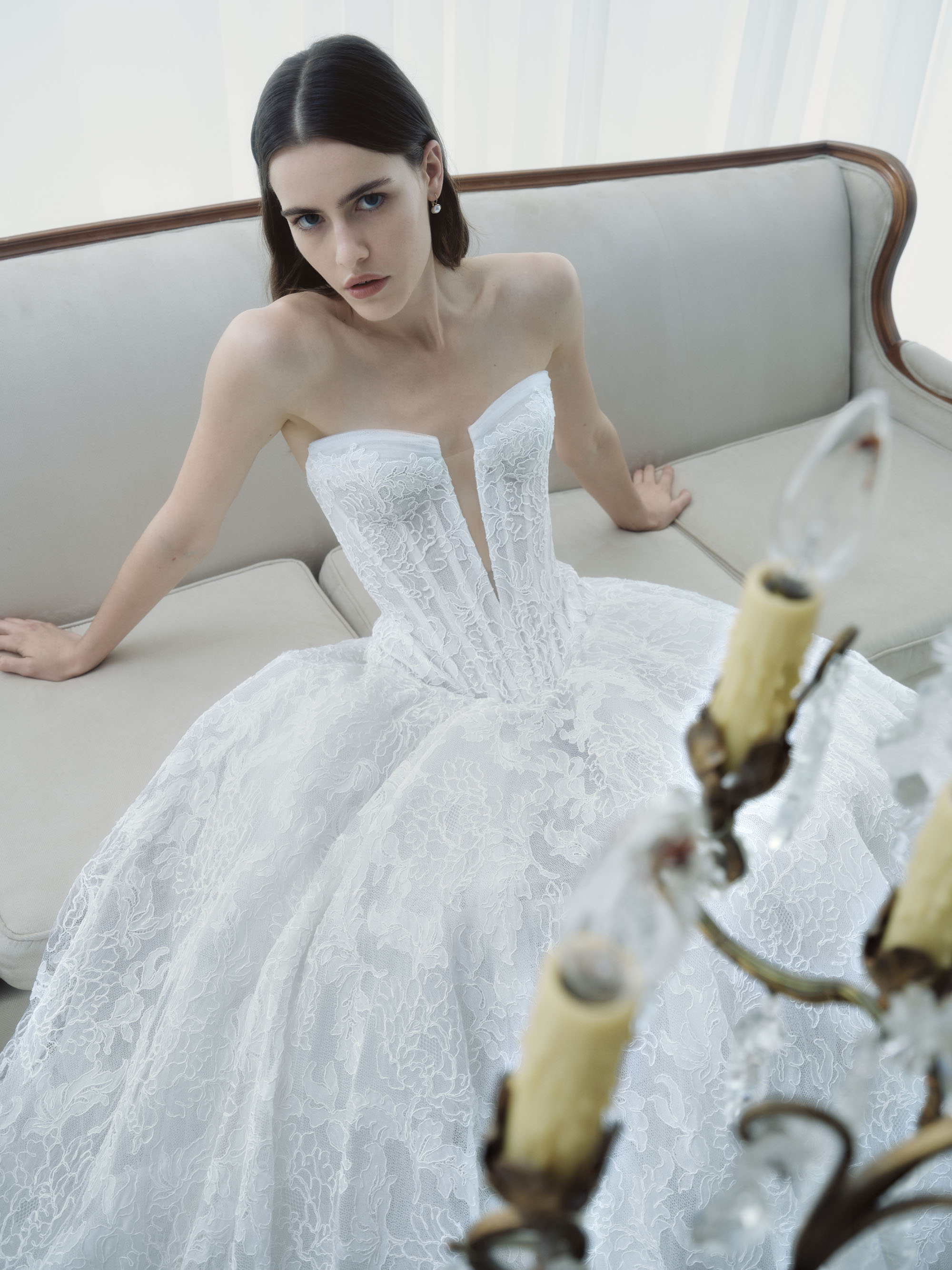 Radiance RIVINI FW26 basque-waist ball gown in Chantilly corded lace with a deep V-neck corset and draped tulle, shown seated.