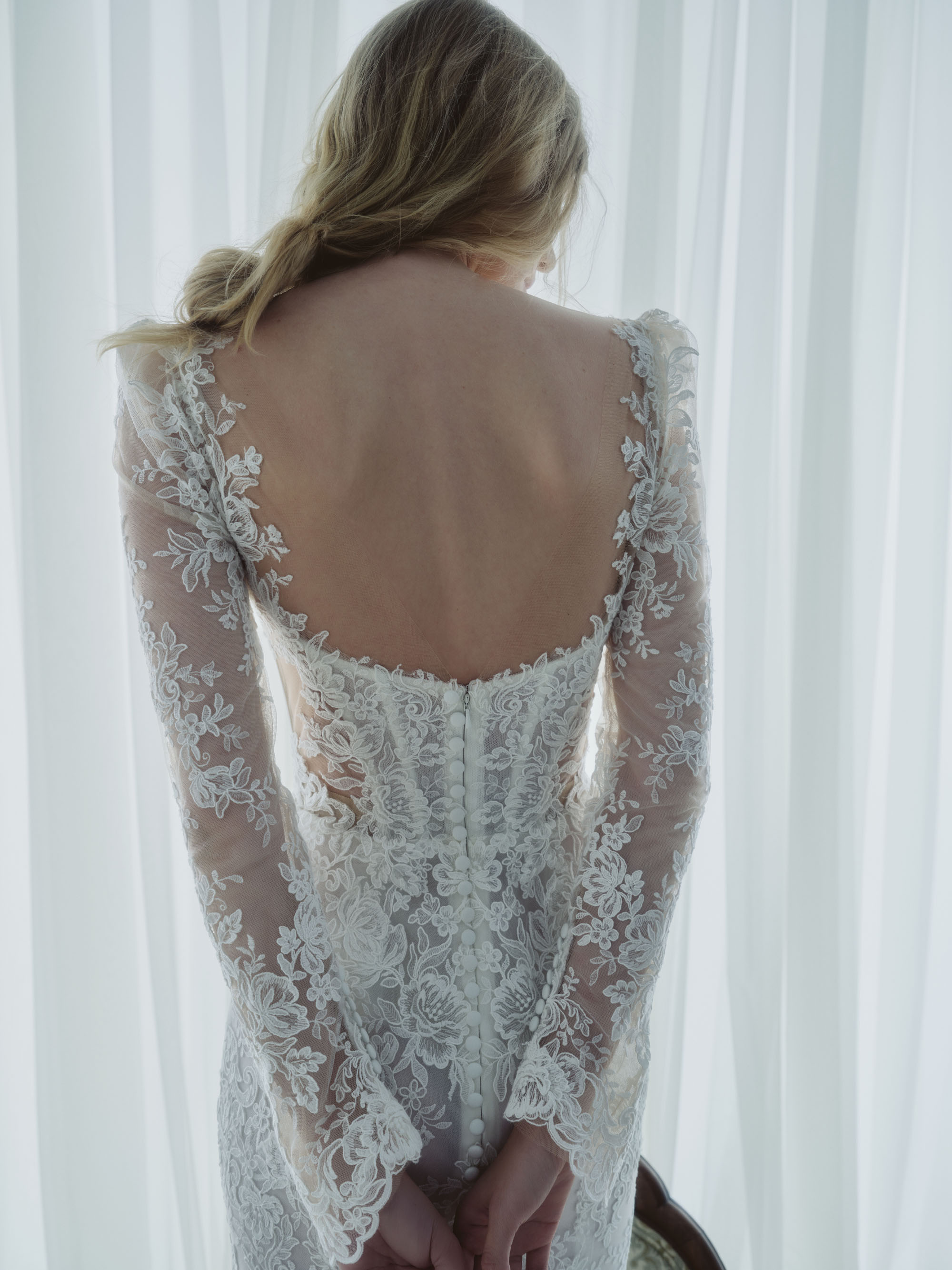 Back view of Serenade showing the sculpted lace sleeves, open back, and buttons extending down the gown.