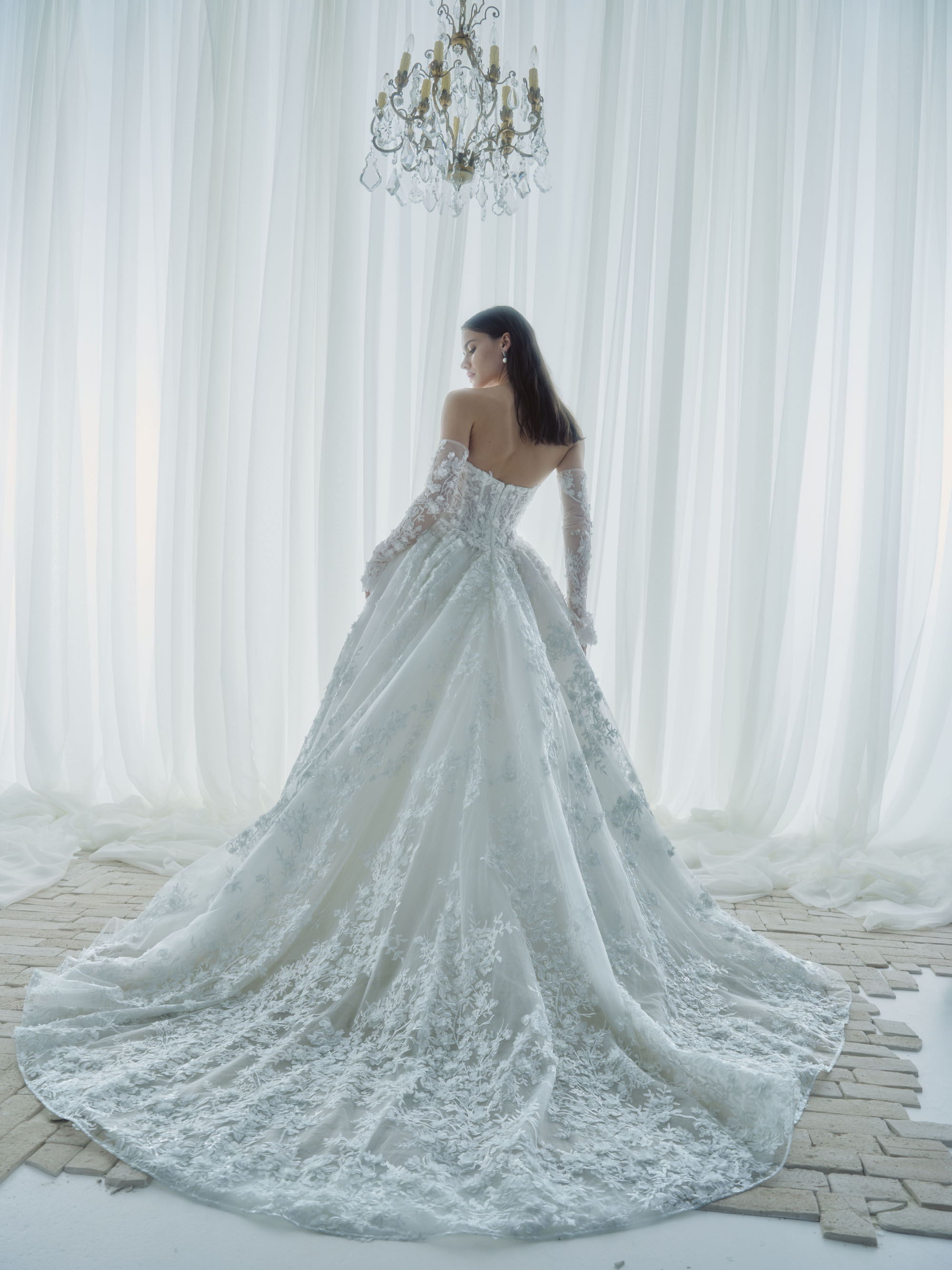 Back view of Whisper showing the fitted corset bodice, dimensional floral lace, and sweeping train.