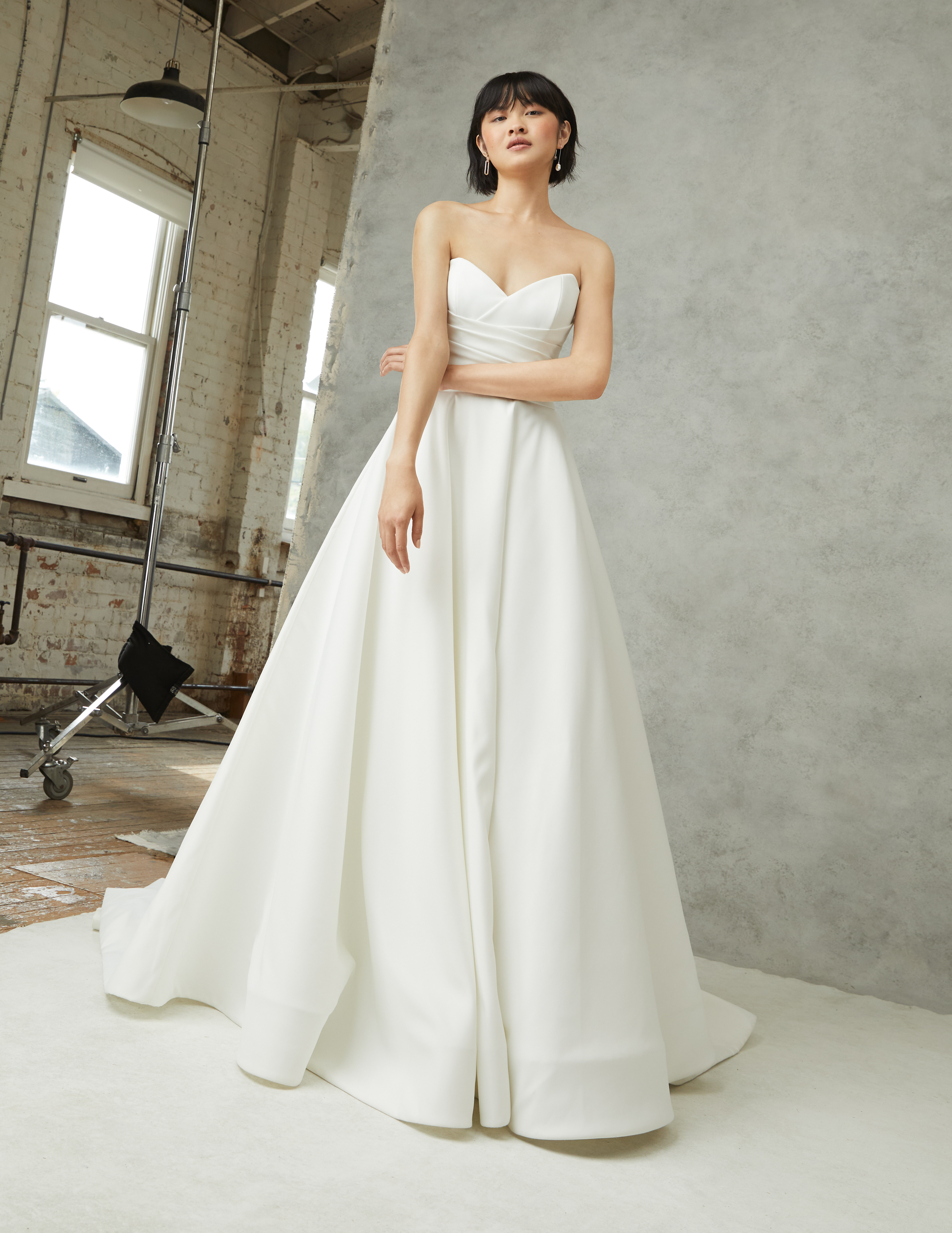 Lena ivory matte satin A-line ball gown with draped cross-over neckline and grand bow, shown from the front.