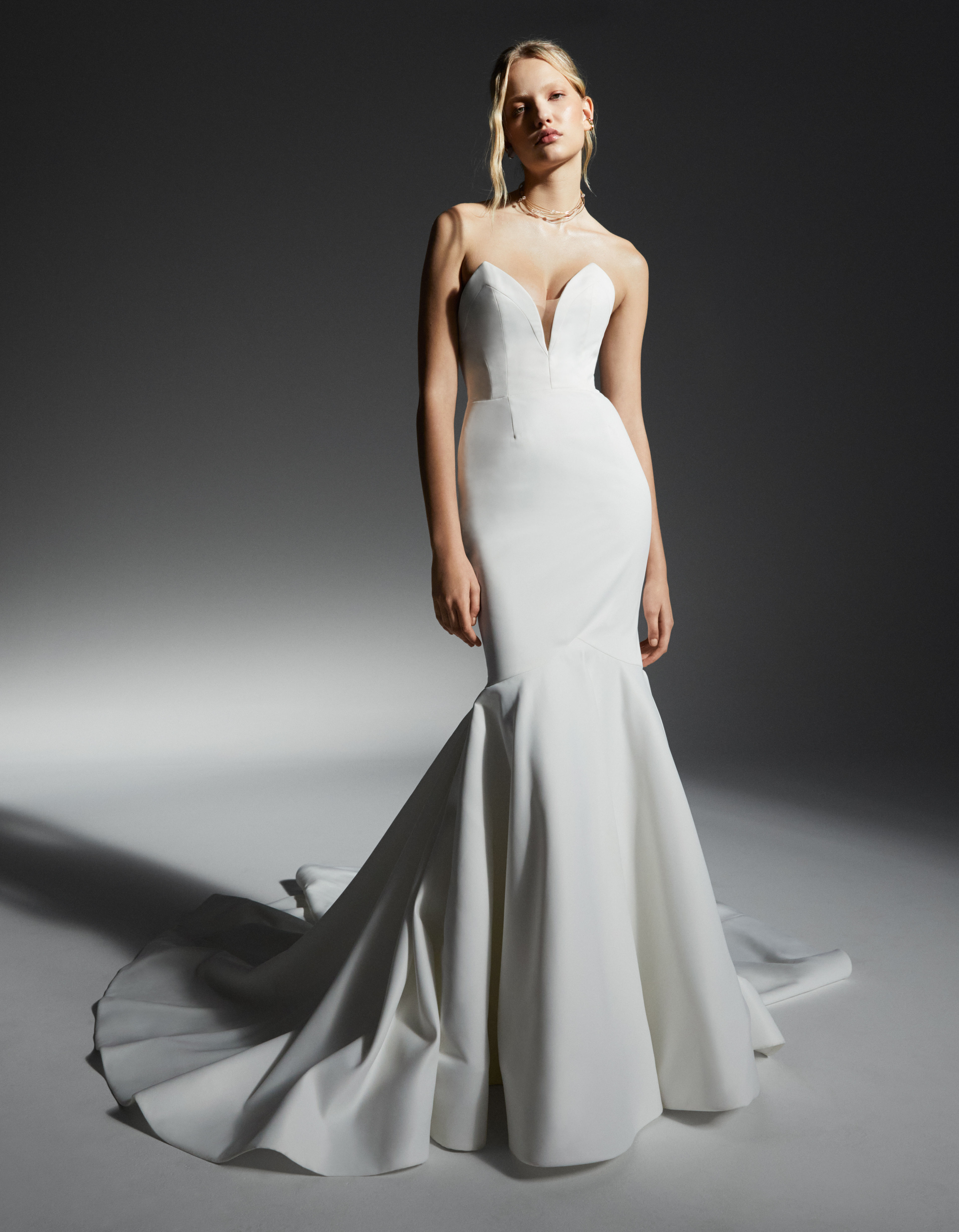 Hanna sculpted strapless fit-and-flare gown with V neckline, pleated gore back skirt detail, and buttons, shown from the front.
