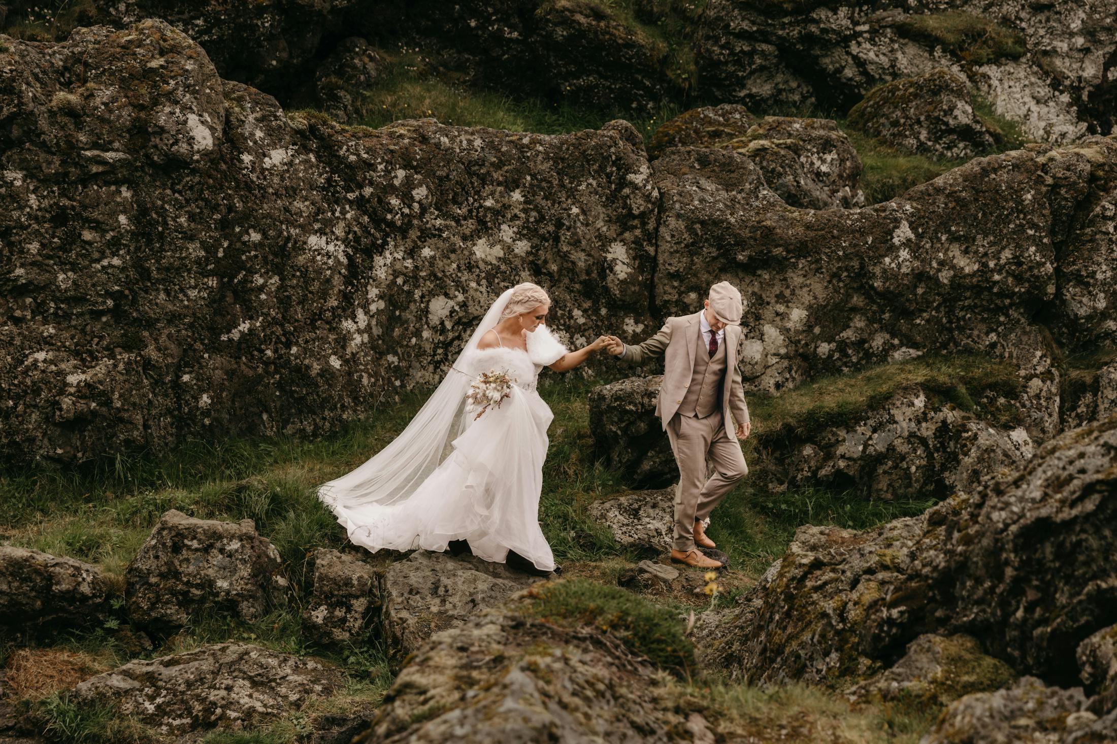 Icelandic bride and groom walking down rocks on he coast of the Snæfellsnes Peninsula in Iceland