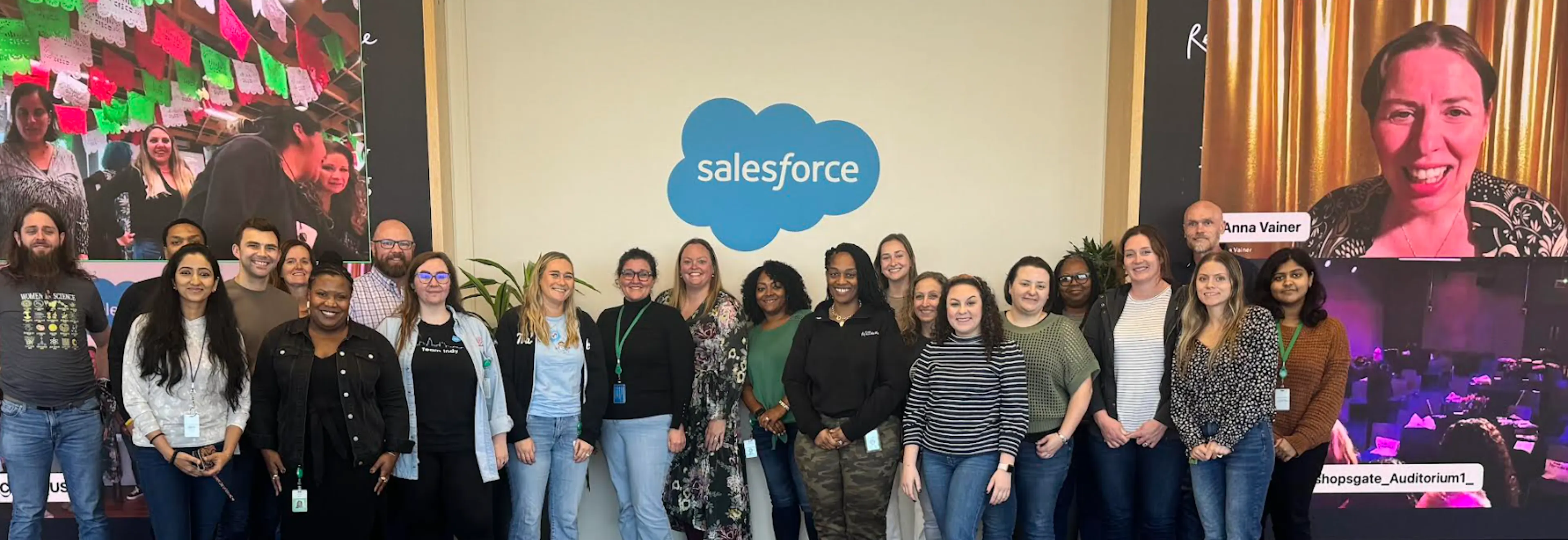 A diverse group of smiling colleagues stand in front of the blue and white salesforce logo