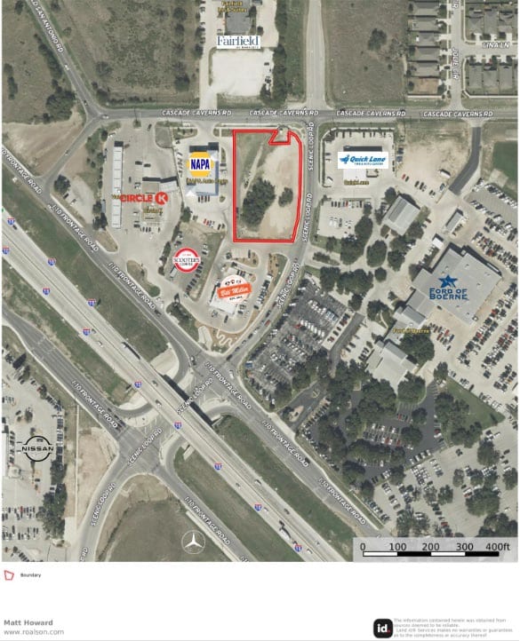 Aerial view of a cleared corner outlined in red at Cascade Caverns Road and Scenic Loop Road, with a convenience store, an auto-parts store and a car dealership around it