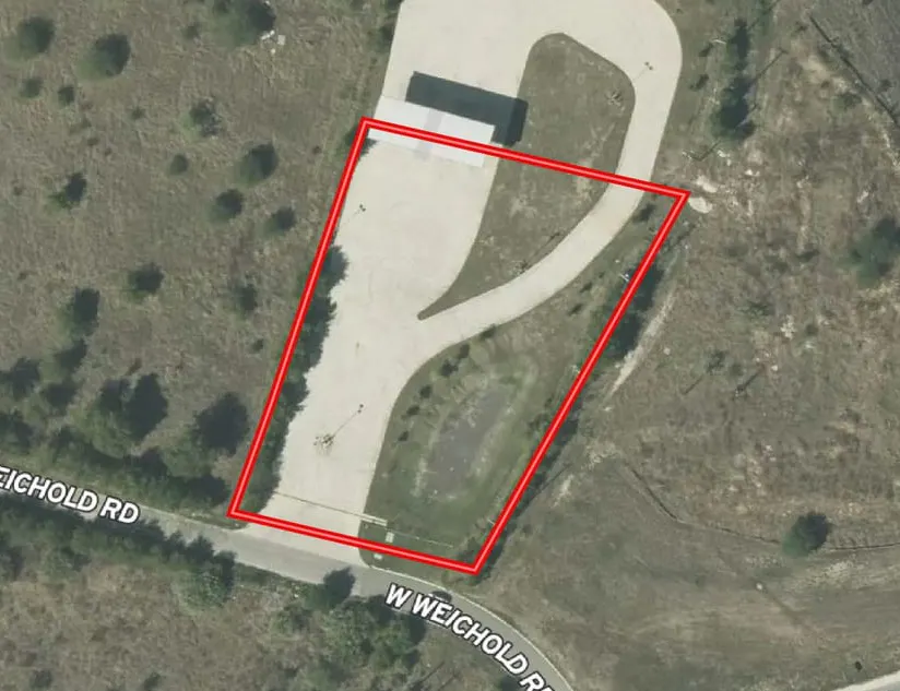 Aerial view of a paved pad site outlined in red on West Weichold Road, off the Interstate 10 frontage at Loop 1604