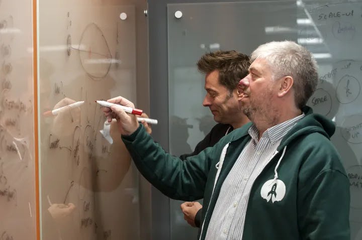 Two people working together writing on a whiteboard