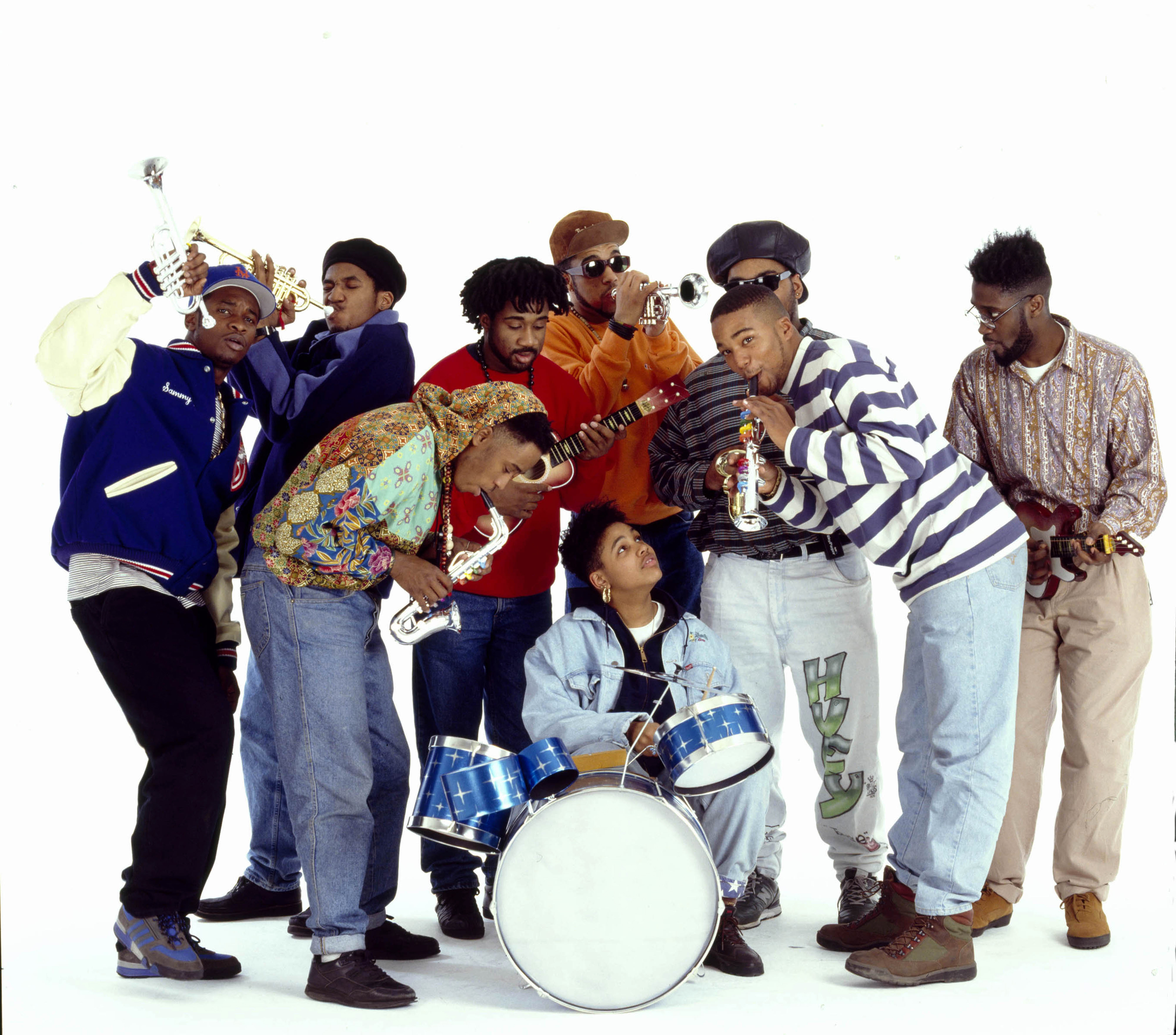 Group portrait of members of the Native Tongues Posse rap collective as they clown around with toy instruments, New York, New York, 1990. Among those pictured are members of the individual groups De La Soul, a Tribe Called Quest, and the Jungle Brothers; this image was taken during the photo shoot for the latter's 'Doin' Our Own Dang' single. Pictured are, from left, DJ Red Alert, Q-Tip, Ali Shaheed Muhammad, Mike Gee (in red), Monie Love (at drums), Afrika Baby Bam, Maseo, and Posdnuos.