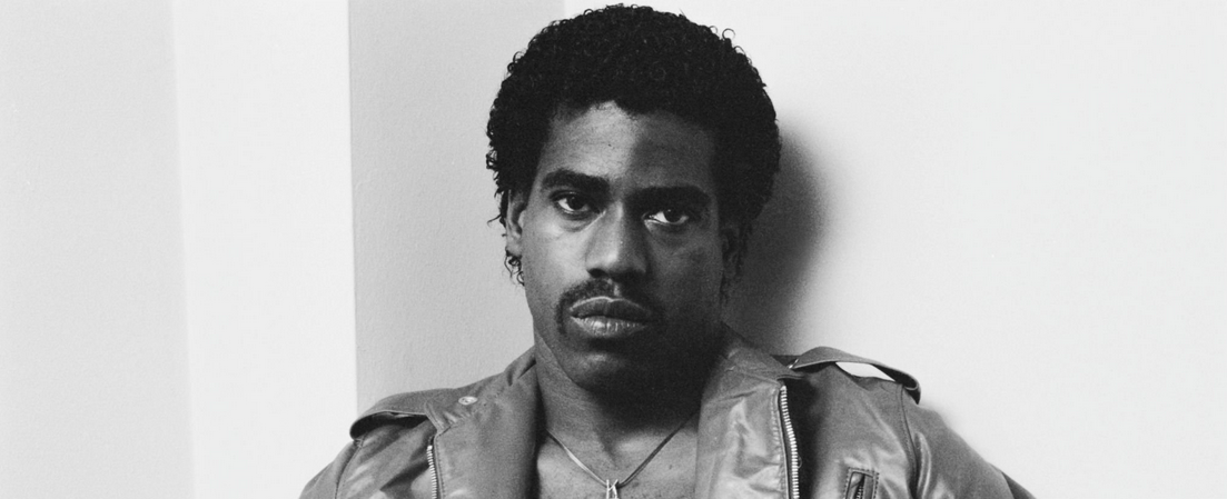 American rapper, singer and songwriter Kurtis Blow wearing a leather jacket over his shirtless torso, a 'KBlow' pendant hanging from his neck, in a studio portrait, location unspecified, circa 1980. 