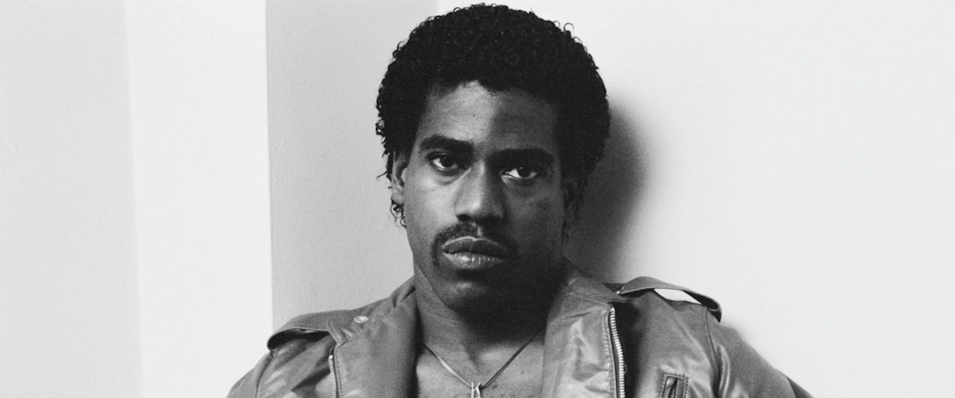 American rapper, singer and songwriter Kurtis Blow wearing a leather jacket over his shirtless torso, a 'KBlow' pendant hanging from his neck, in a studio portrait, location unspecified, circa 1980. 