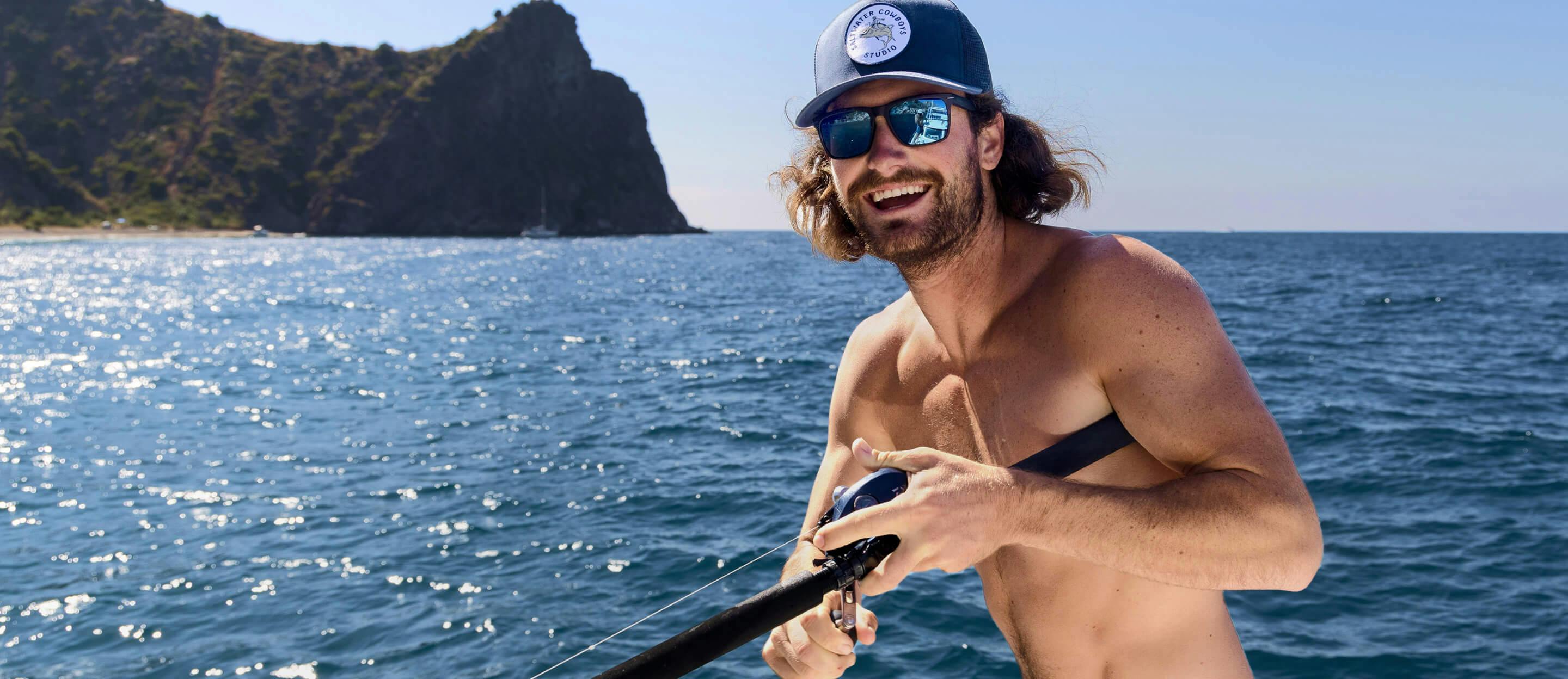 A man fishing wearing thick frames, square, matte black with glacier mirrored sunglasses in the ocean right off the coast of an island.