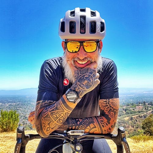 Man with tattoos smiling on a bicycle and ROKA sunglasses with gold lenses