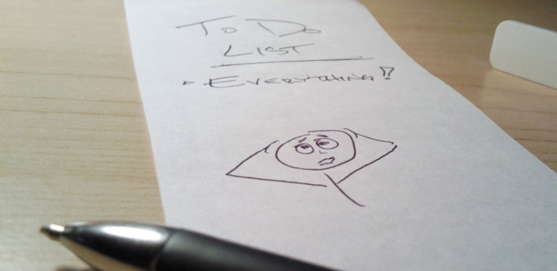 Note and pen sitting on a desk with the words to do list everything written on it with an illustration of a stickman holding his head