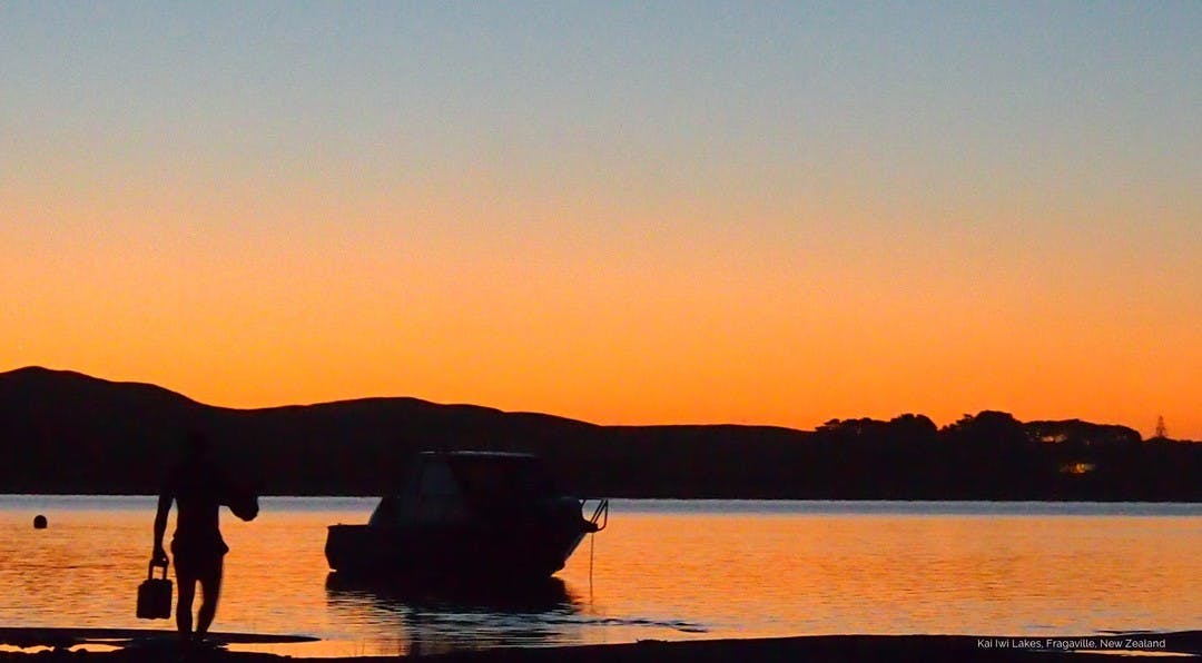 sunset lanscape image with a black silhouette of a man walking to his boat which is moored on the beach.