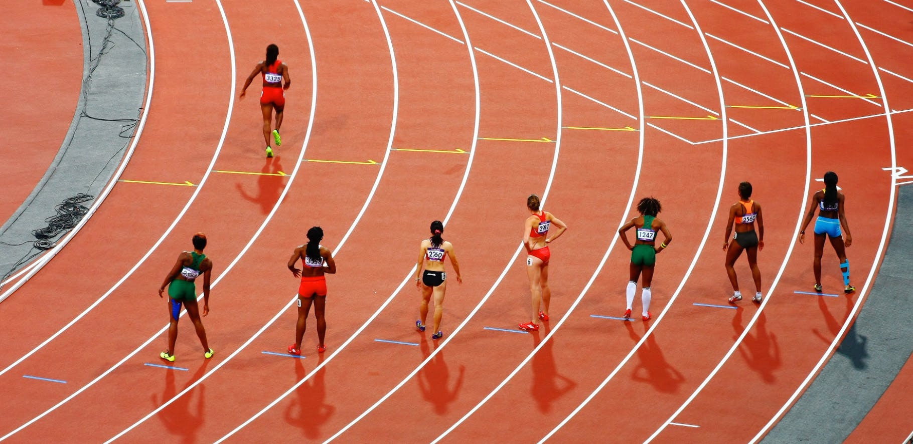 Track and field athletes lining up to start a race while one runner is already off running ahead of everyone else.