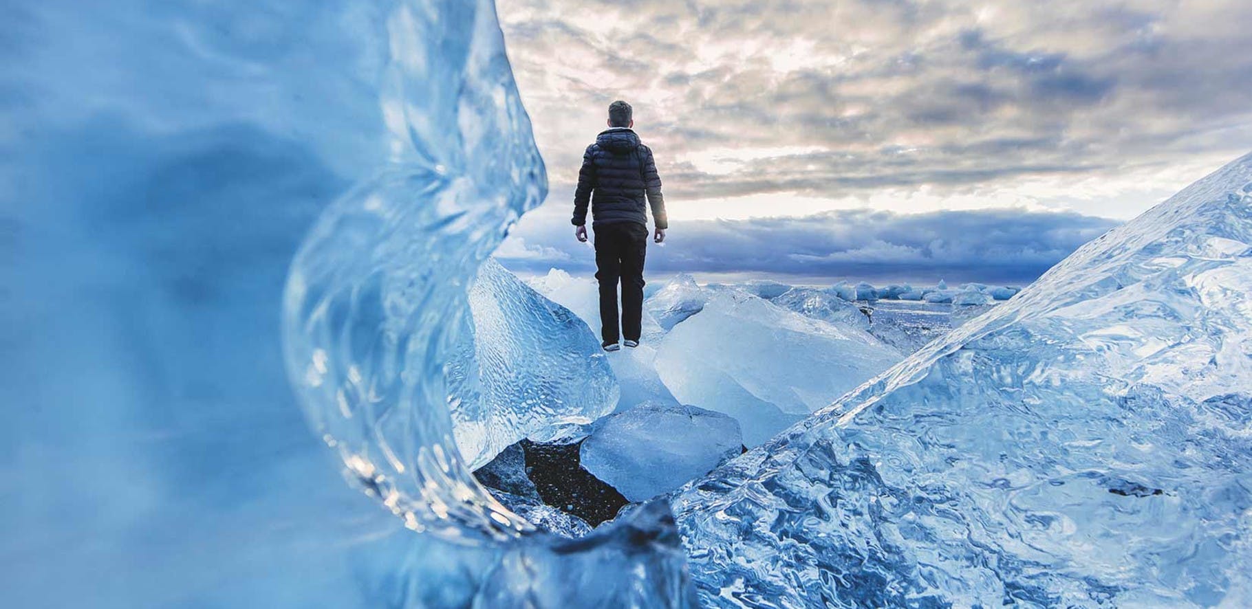 close up image looking through glacier ice, with a man standing in the background looking out over the vast glacier