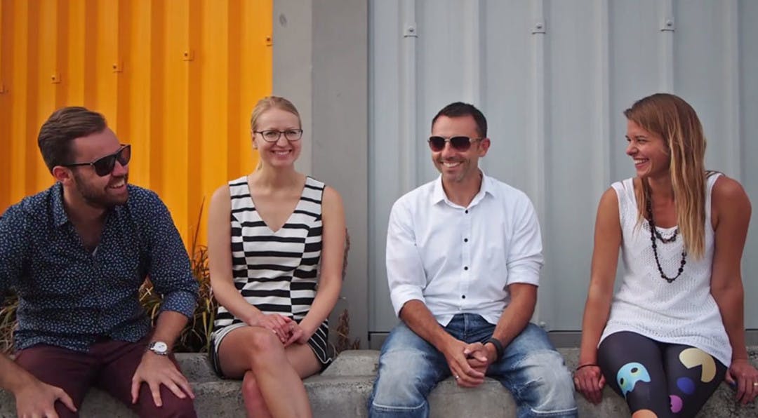 group of 4 people sitting down in an industril area talking and smiling.