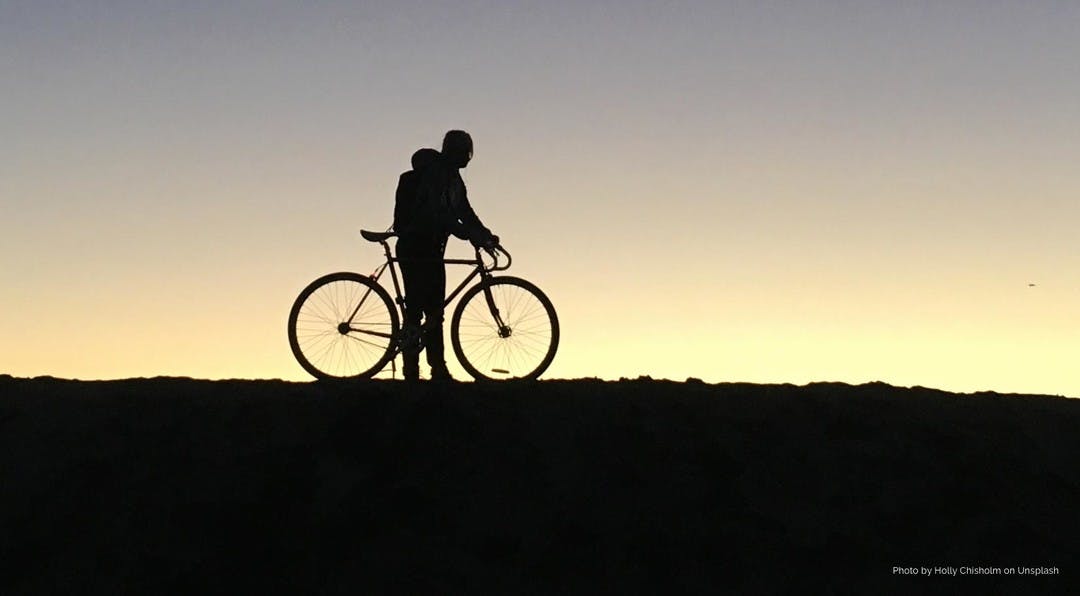Black silhouette of a man and his bicycle against an evening sunset backdrop