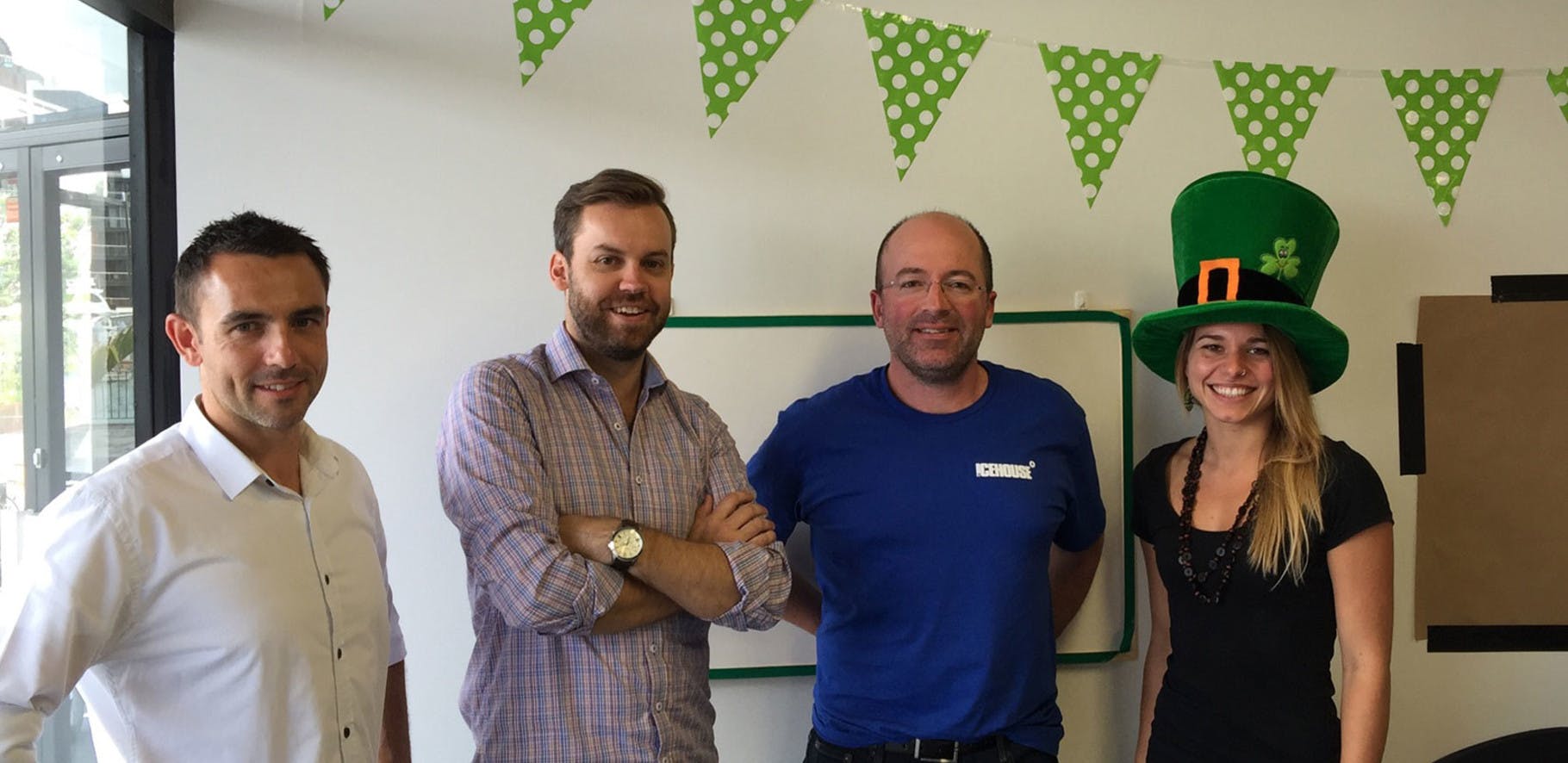 A group of four people are posing in an office along with St Patricks day decorations.