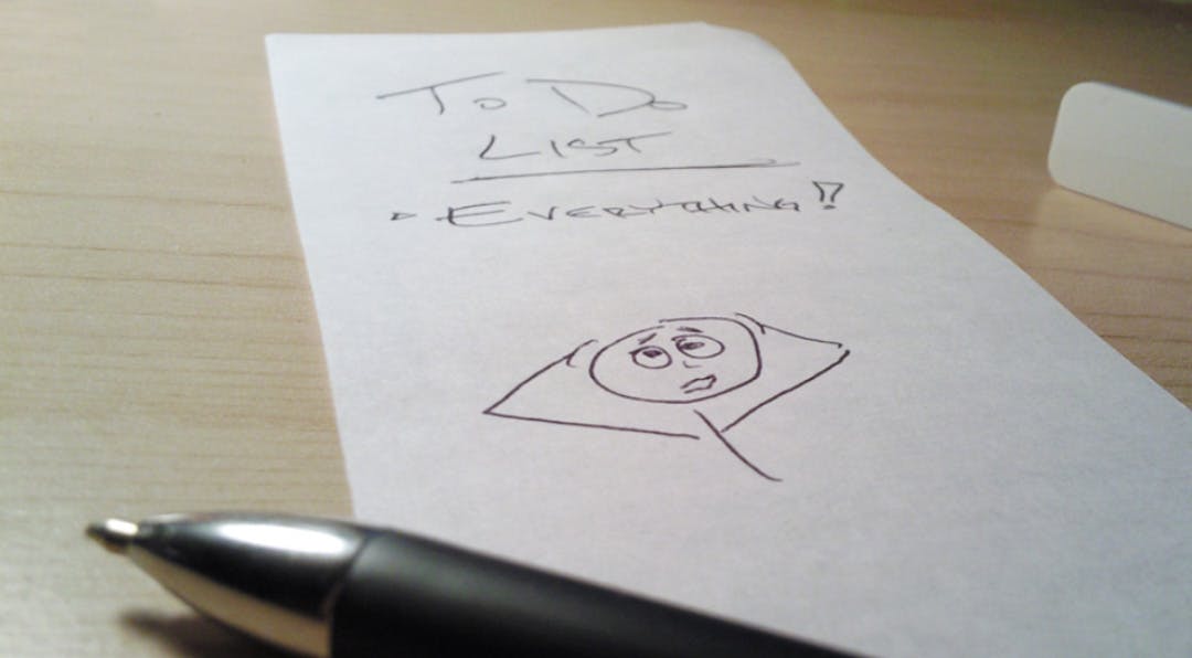 Note and pen sitting on a desk with the words to do list everything written on it with an illustration of a stickman holding his head