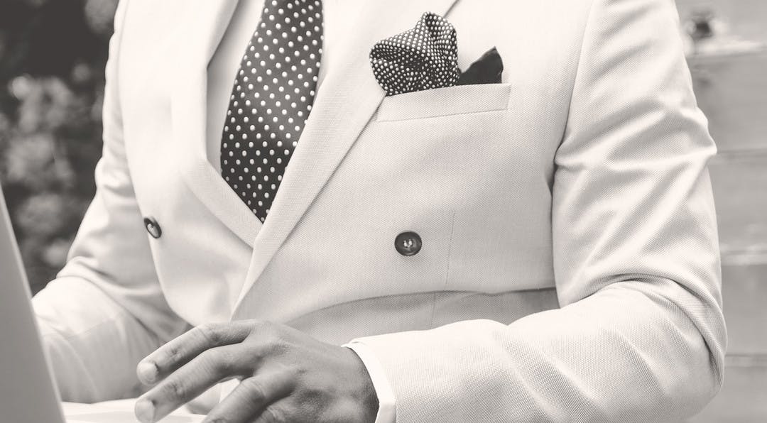 black and white image of a man wearing a classy white suit using a laptop.