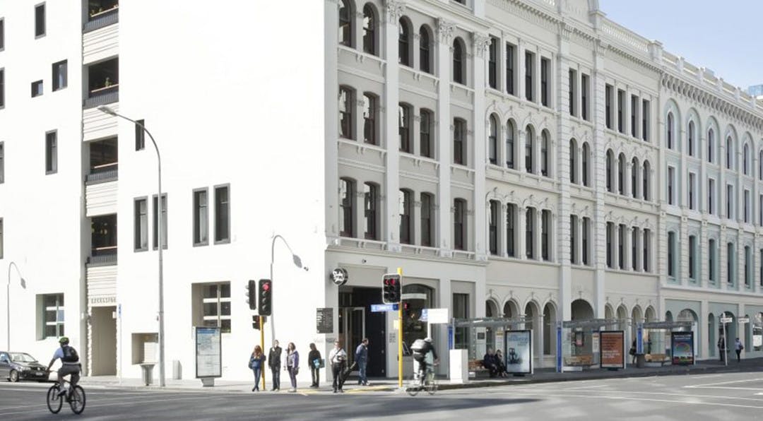 people standing on a street corner waiting for the lights with a big building behind them