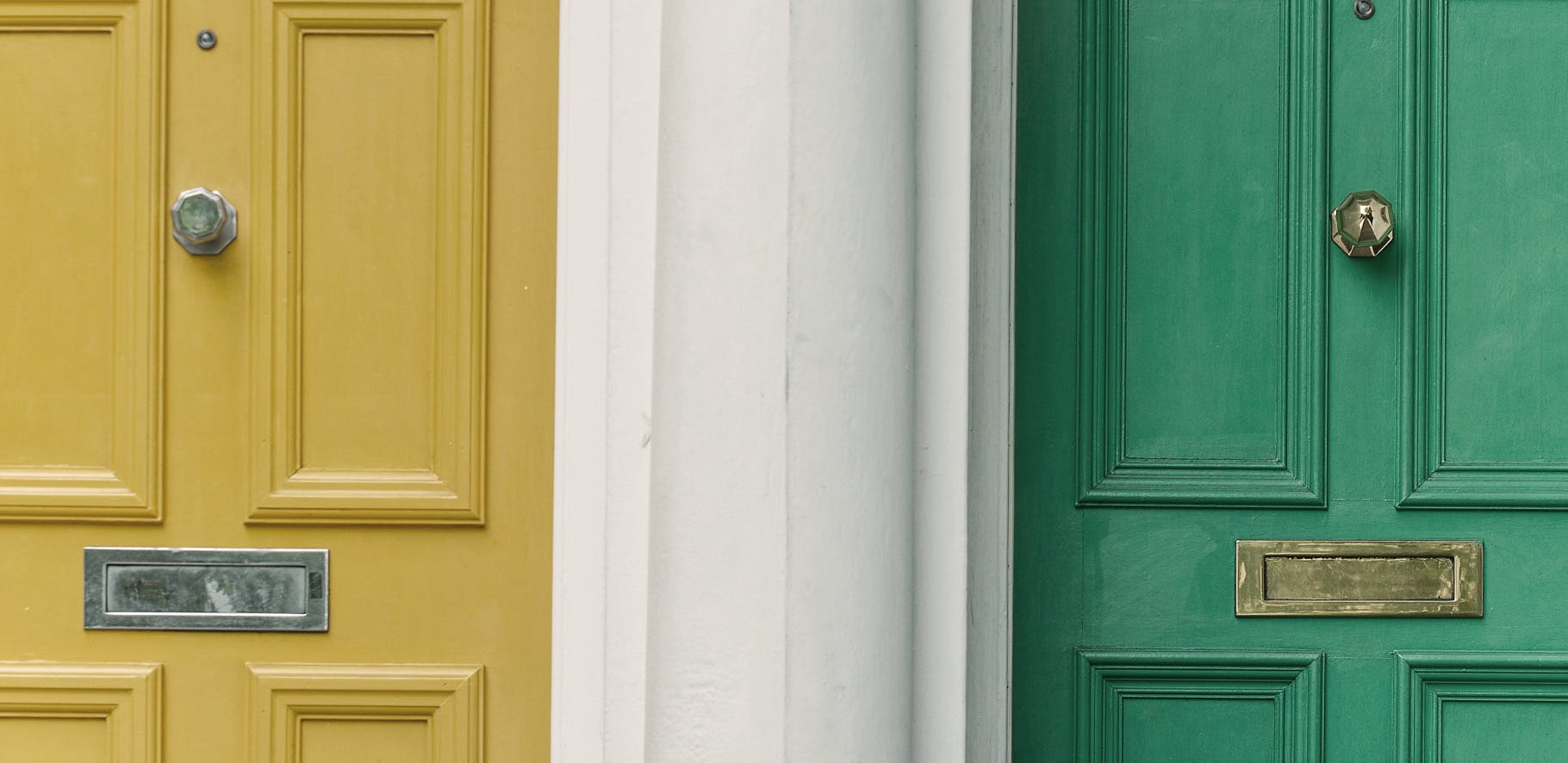 two doors are seperated by a white wall, there is a yellow door on the left and a green door on the right.