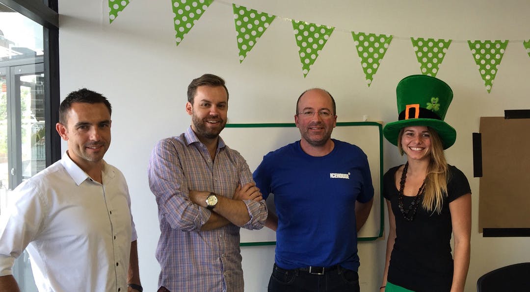 A group of four people are posing in an office along with St Patricks day decorations.