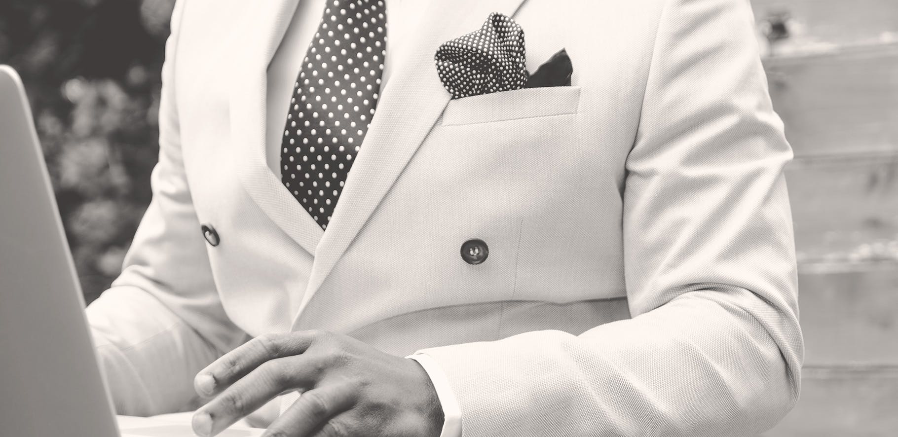 black and white image of a man wearing a classy white suit using a laptop.