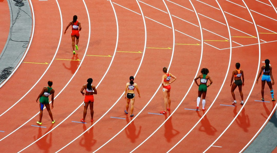 Track and field athletes lining up to start a race while one runner is already off running ahead of everyone else.