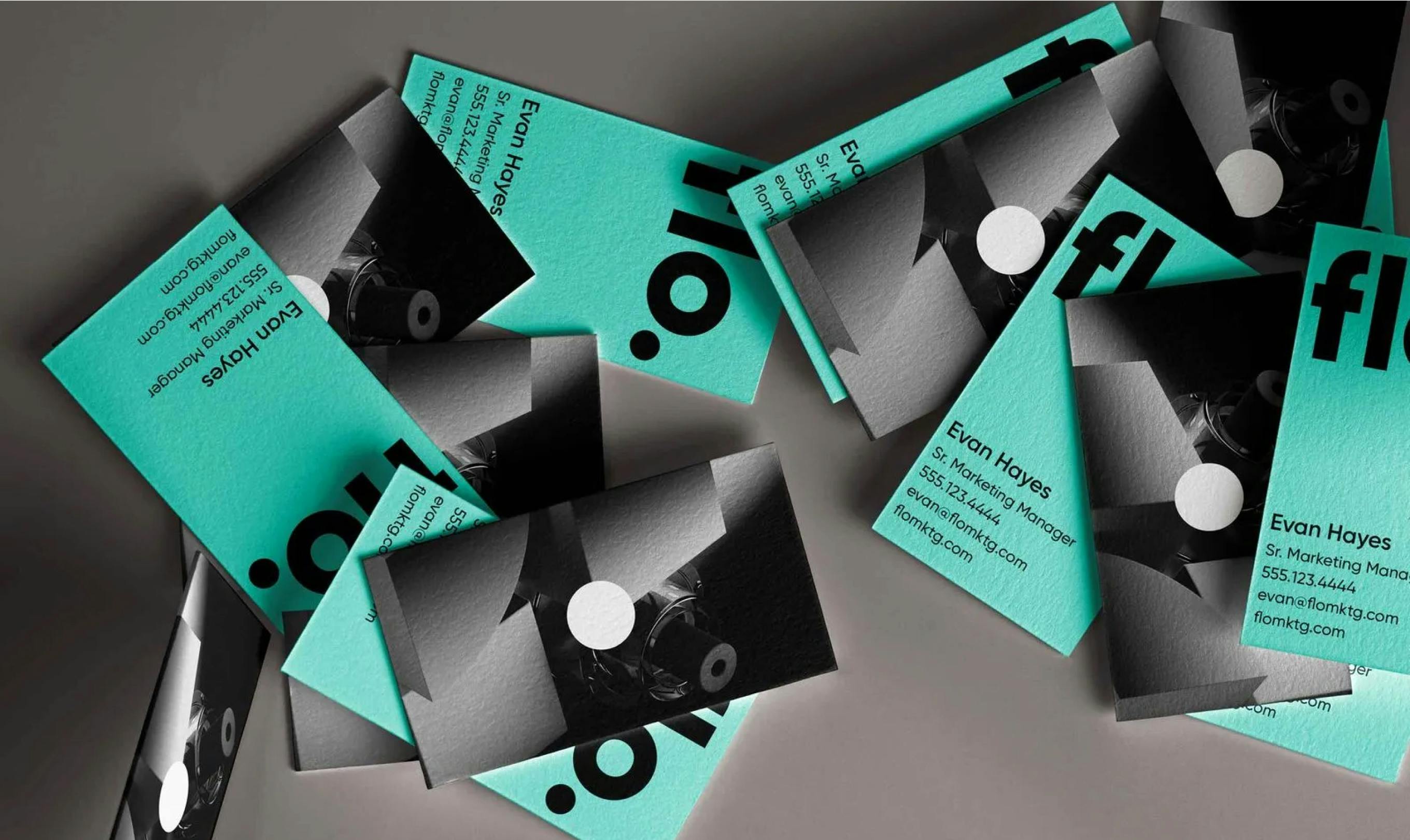 Flo business cards--one side Mint with employee information, and one with a black and white 3D icon render--scattered on a gray table.