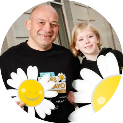 Rory best smiling with a child, holding Cancer Fund For Children flowers.