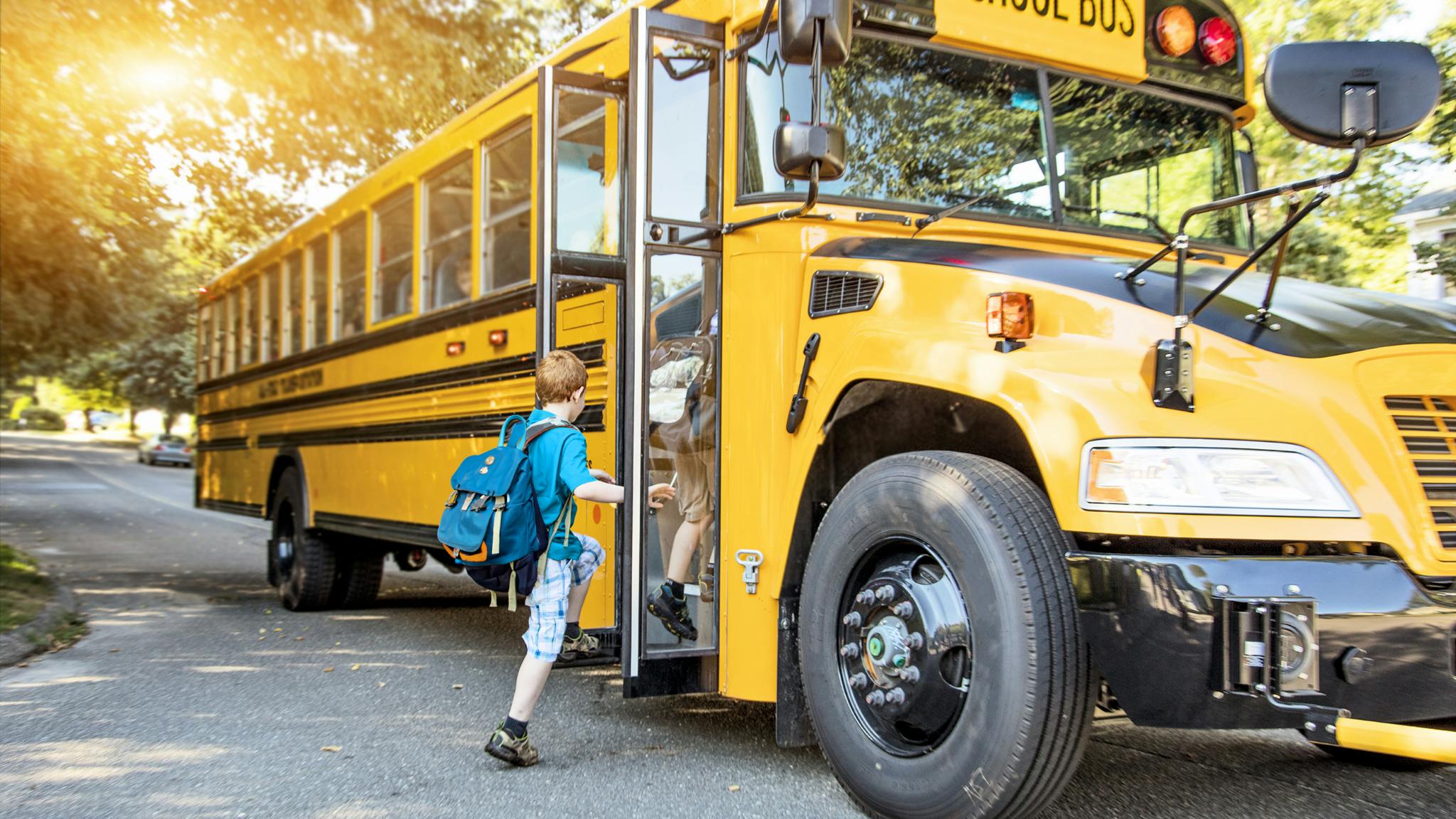 Child with blue backpack boarding a yellow school bus, promoting school transportation safety.