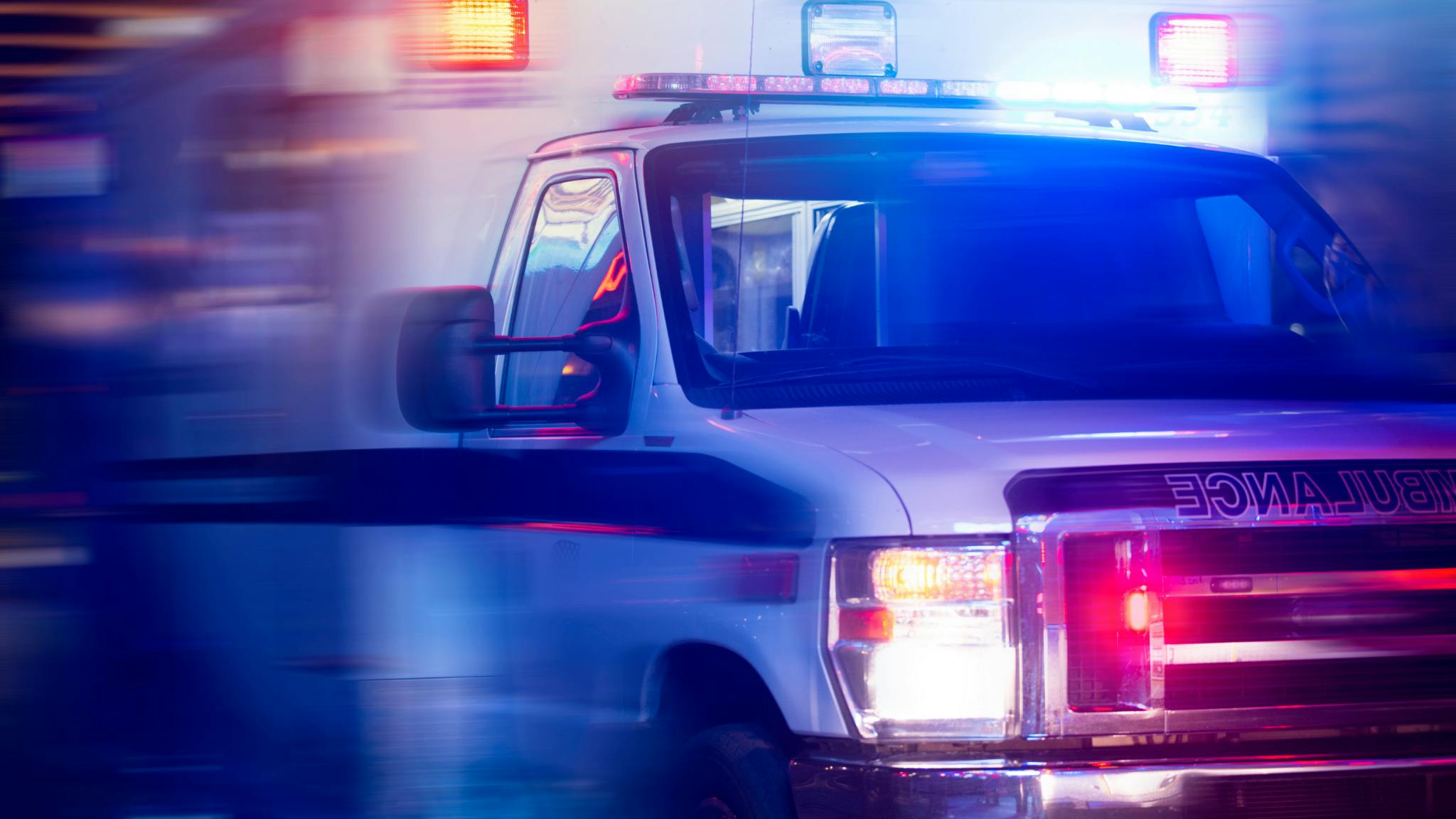 Ambulance with flashing lights driving on a road at night, highlighting emergency response and vehicle safety.