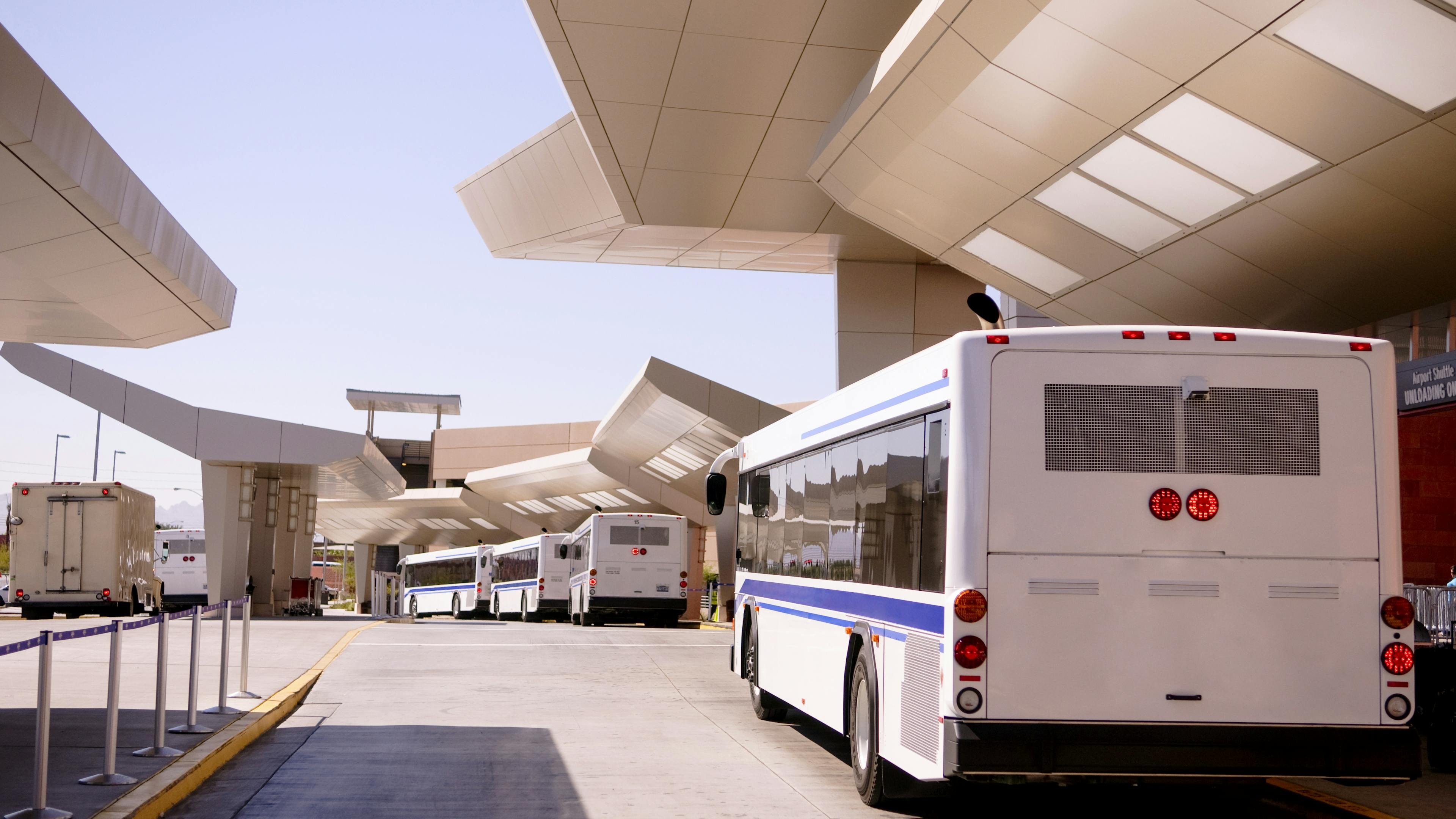 White buses parked beneath a sleek, angular terminal on a clear day.