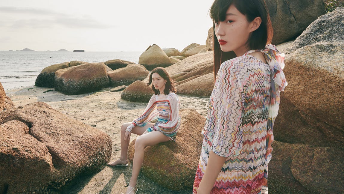 There were two young ladies at the beach wearing colorful clothing.