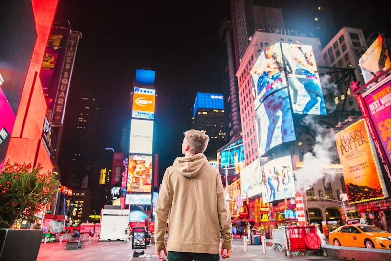 A young man walking on a busy street at night looking at colorful signboards.