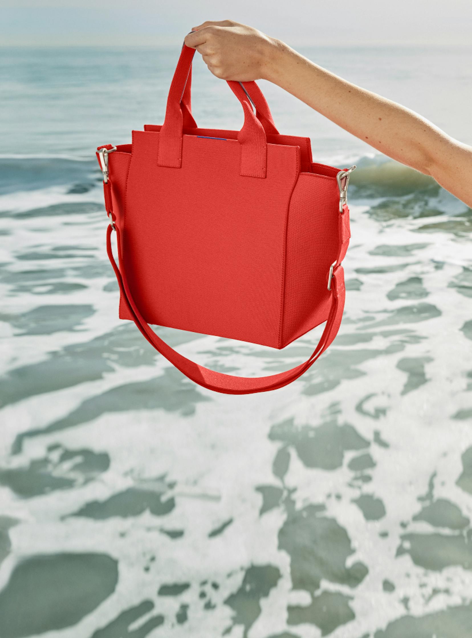 Model holding The Handbag in Bright Poppy by the ocean.